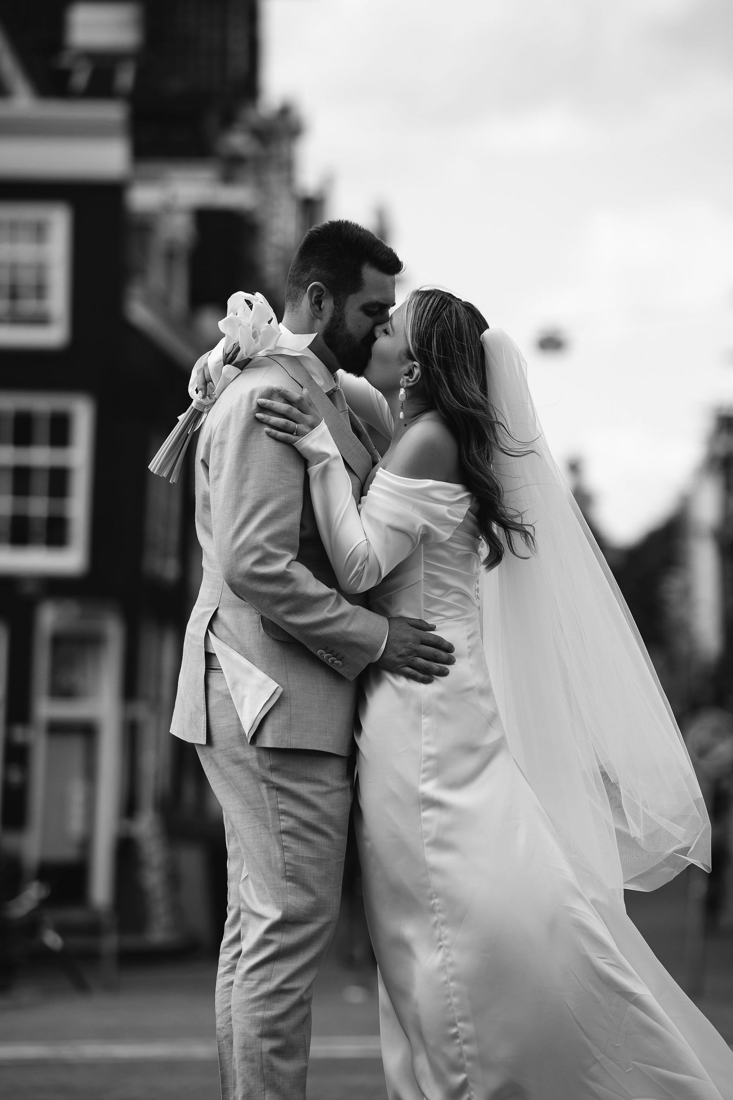 A romantic black and white wedding photo of newlyweds sharing their first kiss on an urban street.