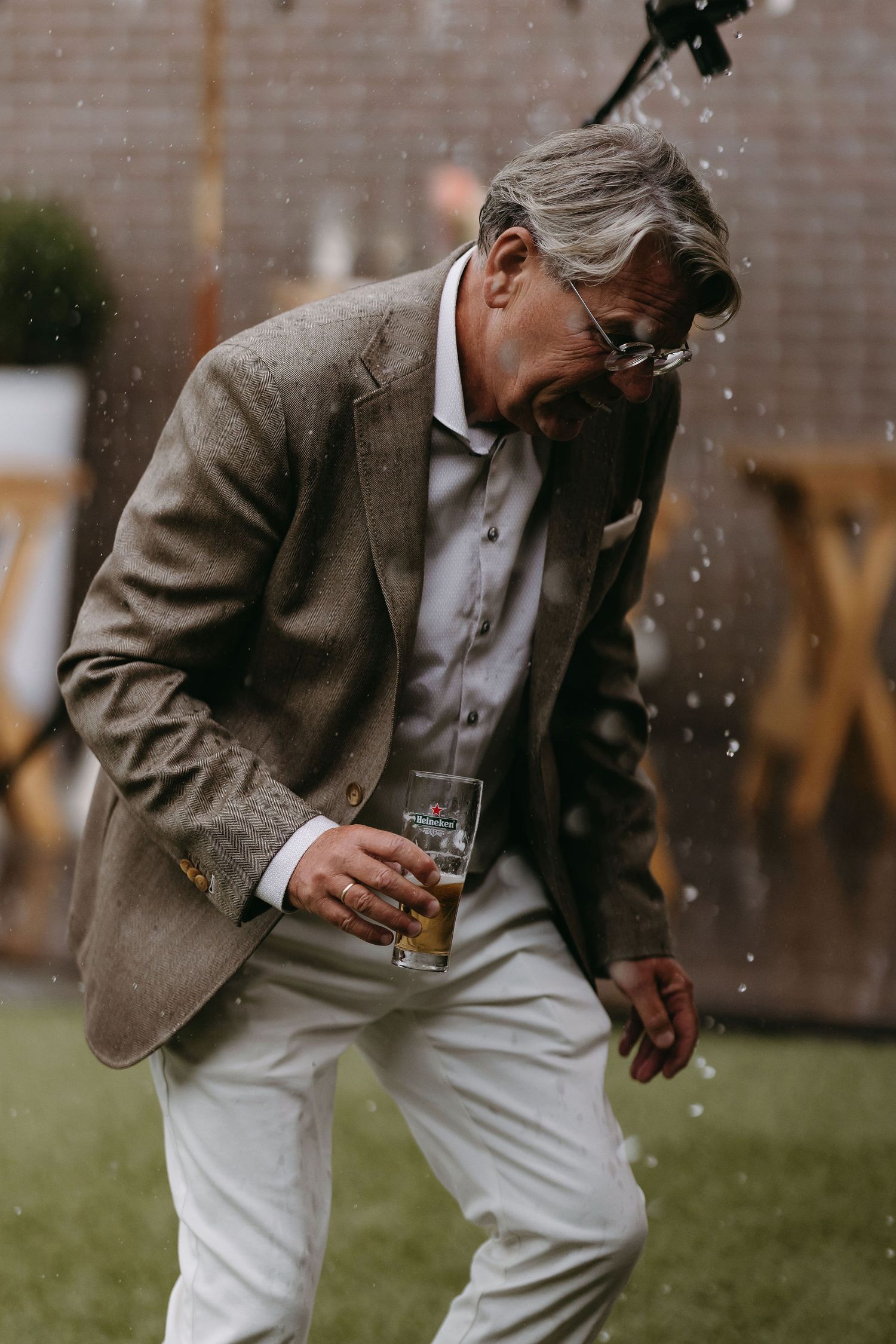 Person in tweed jacket playfully dancing with drink at outdoor celebration.