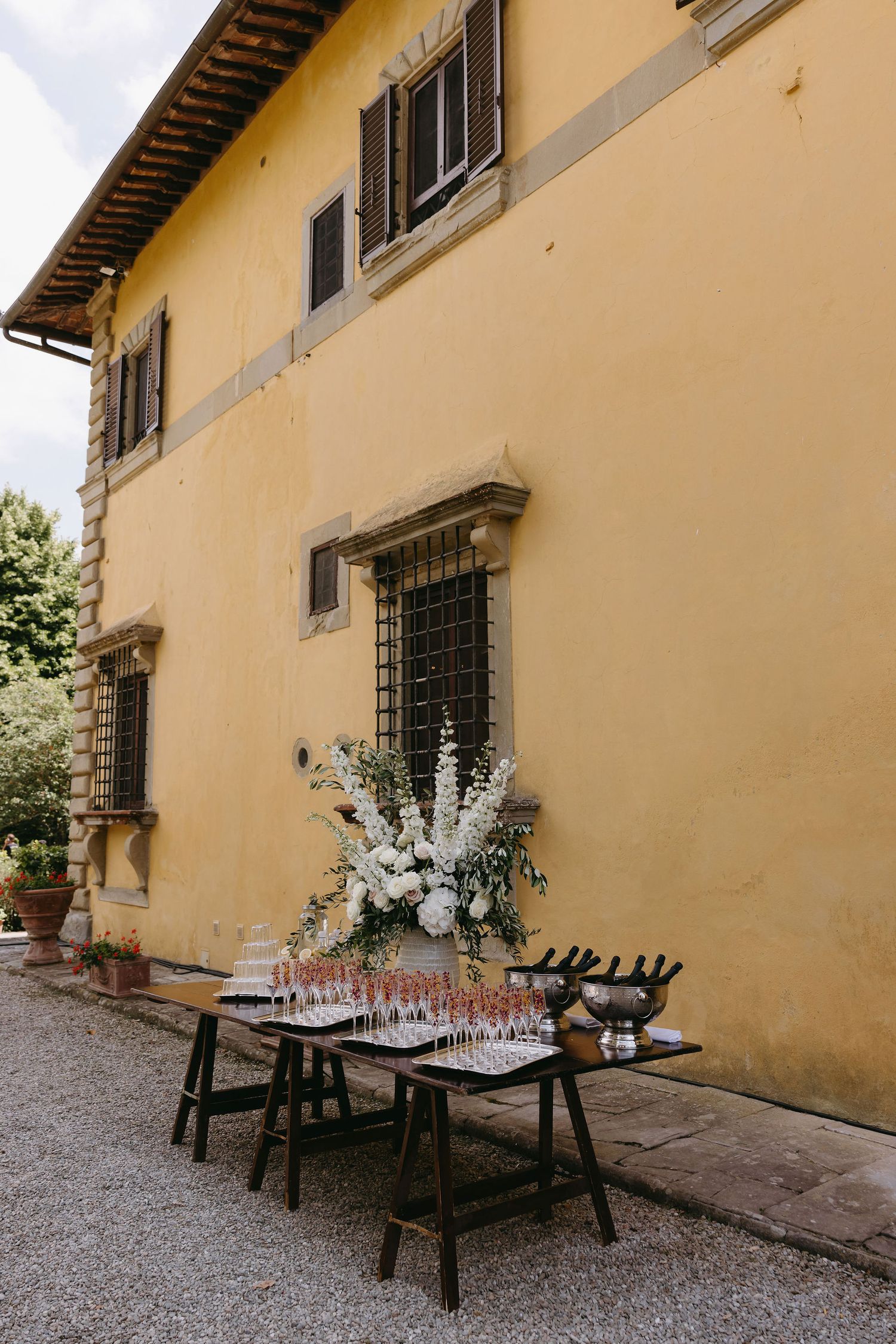 Rustic outdoor venue setup with wooden tables against a yellow Mediterranean-style building facade.