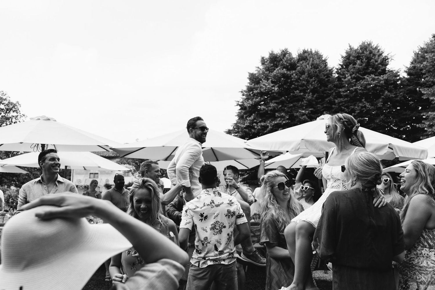 Black and white photo of wedding guests celebrating under white tents outdoors.