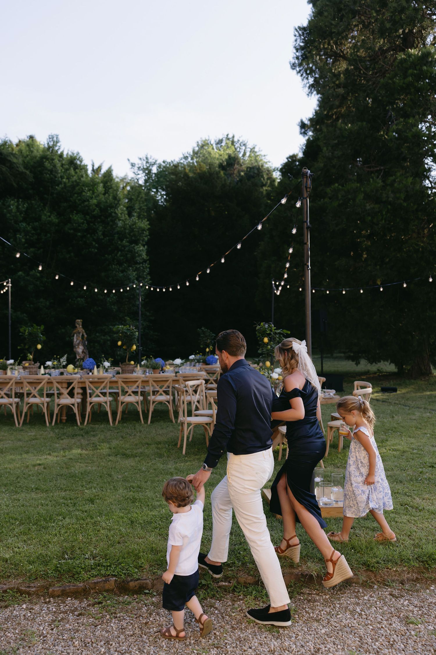 Outdoor evening celebration with string lights and people dancing on a gravel path.