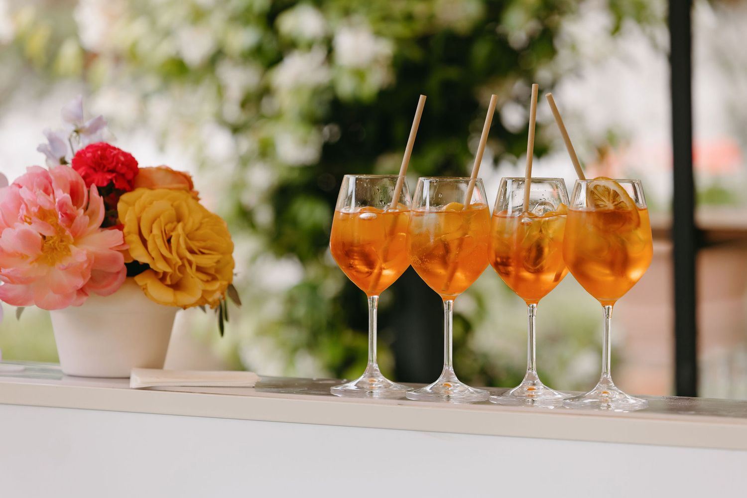 Row of Aperol Spritz cocktails with orange roses in a vase.