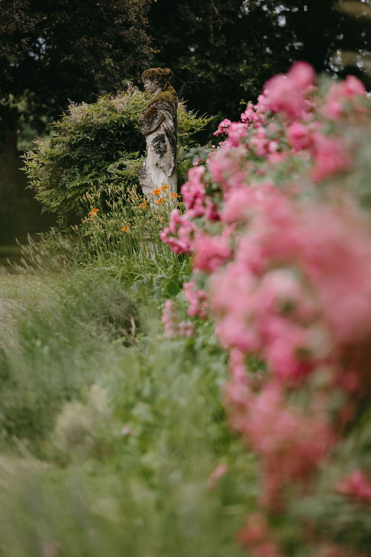 Garden statue nestled among pink flowers and wild grasses.