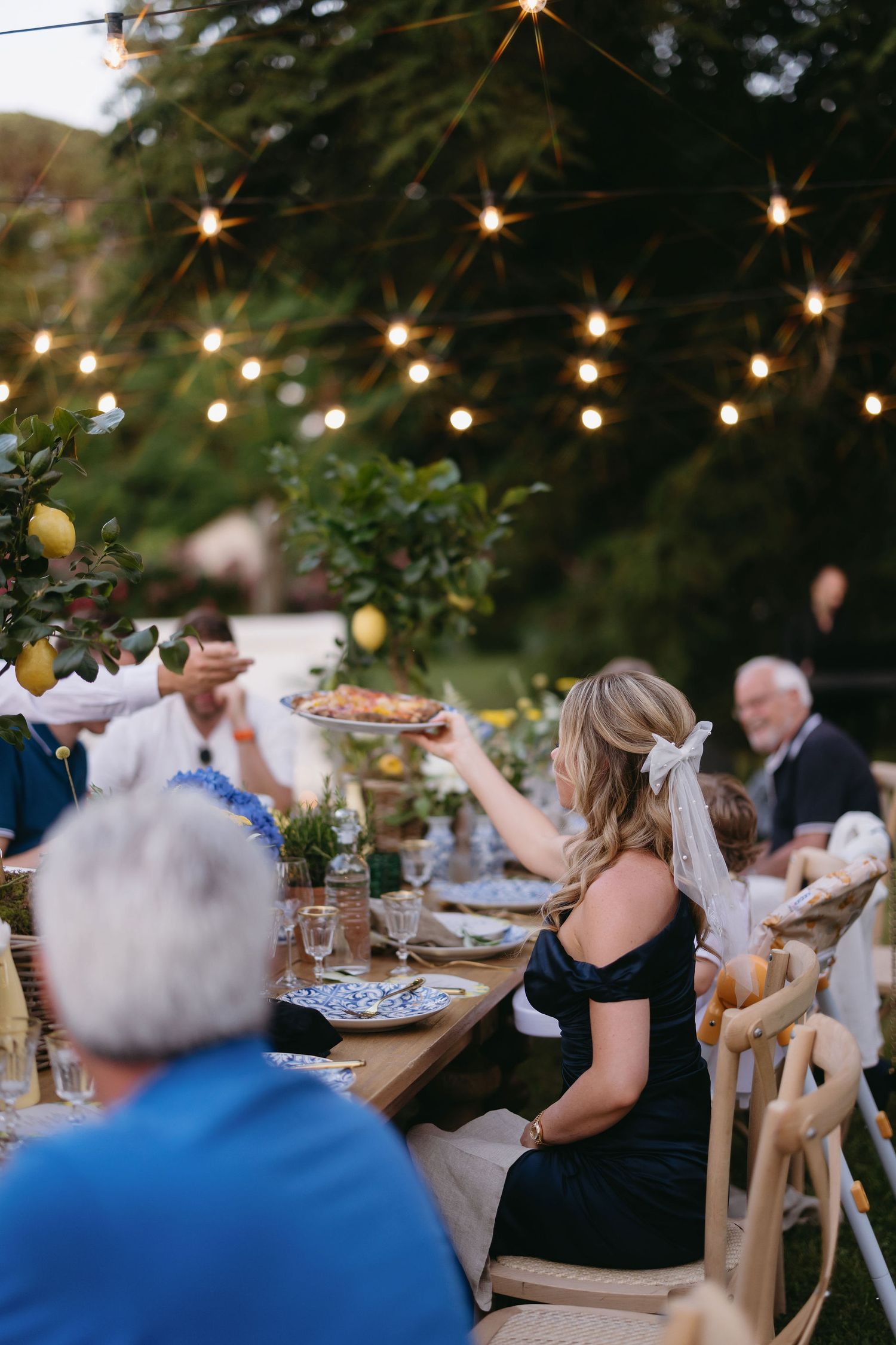 Outdoor wedding reception with string lights and rustic table settings at dusk.