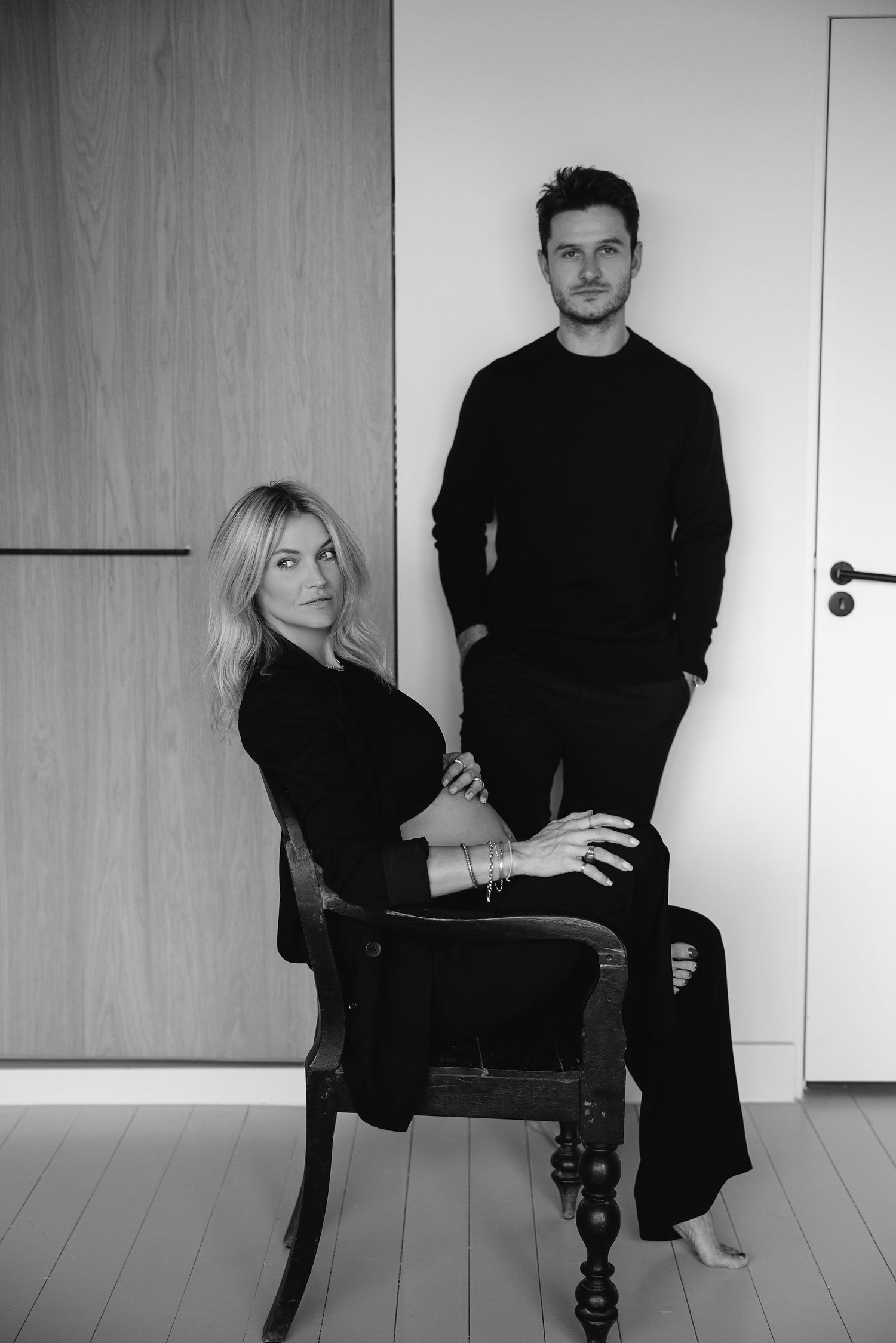 Stylish black and white maternity photo with couple posing against white wall.