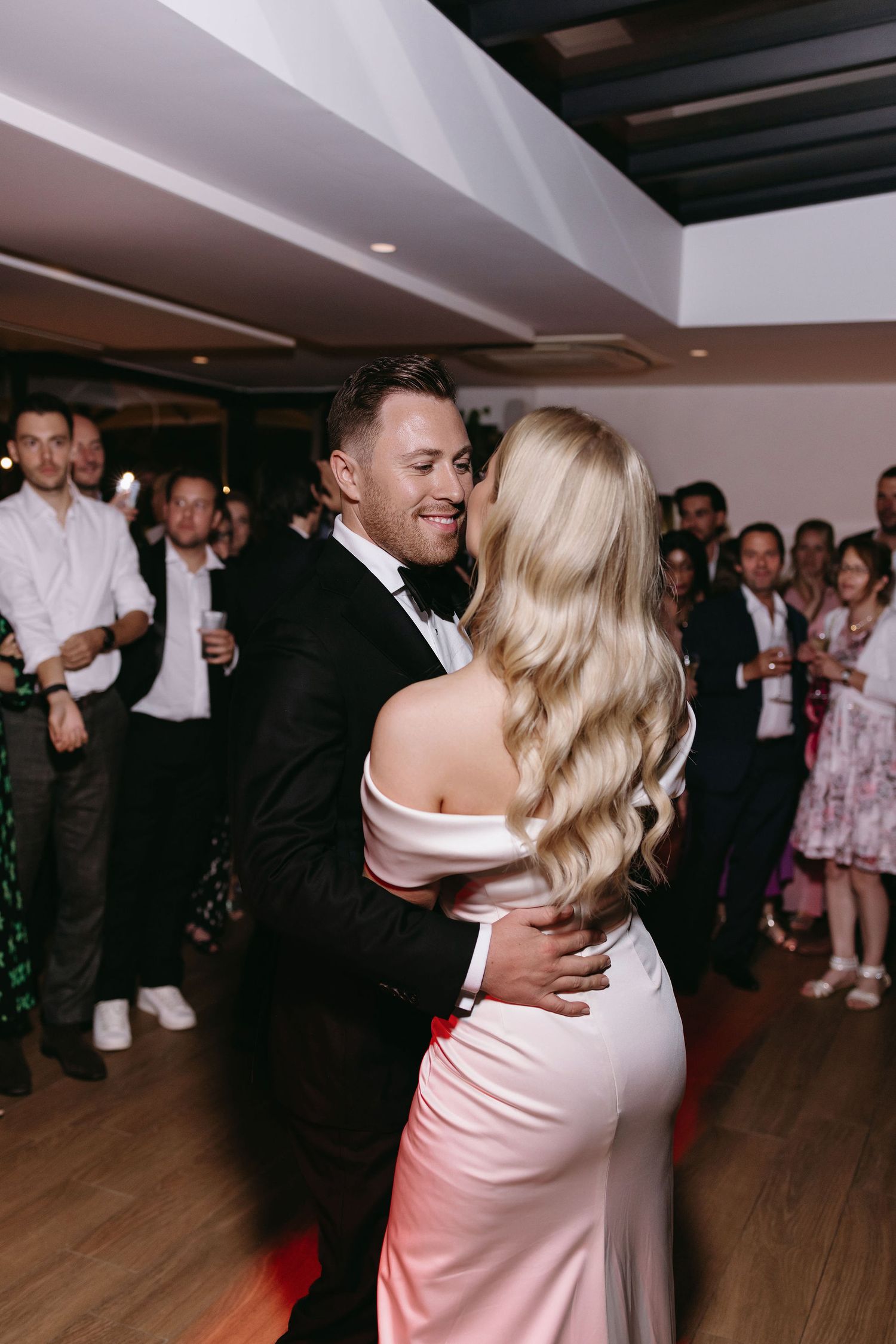 Wedding couple shares an intimate dance during their reception as guests look on.