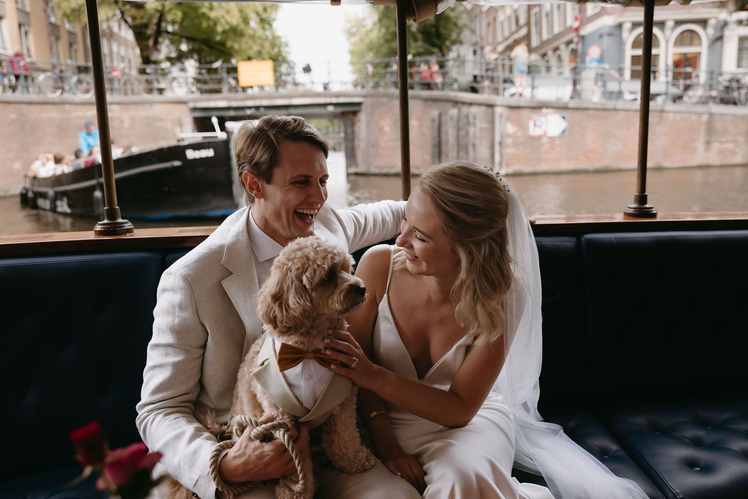 Newlyweds share intimate moment with small dog on boat in Amsterdam canal.
