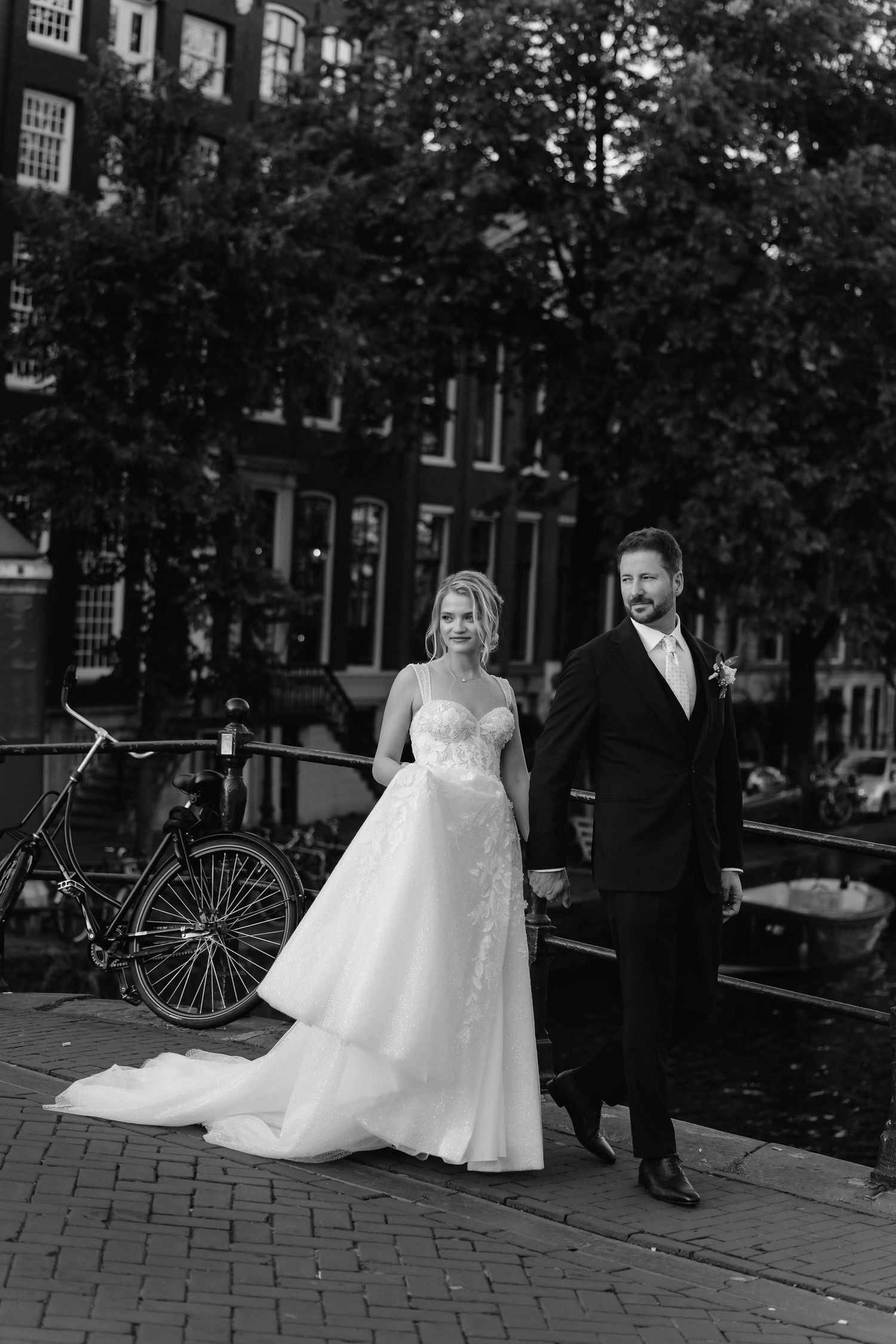 Black and white portrait of newlyweds standing on Amsterdam street with bicycle in background.