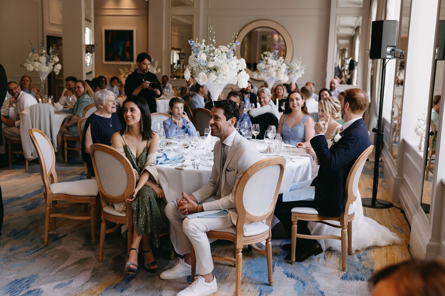 Elegant wedding reception dining room filled with guests seated at round tables with white tablecloths.