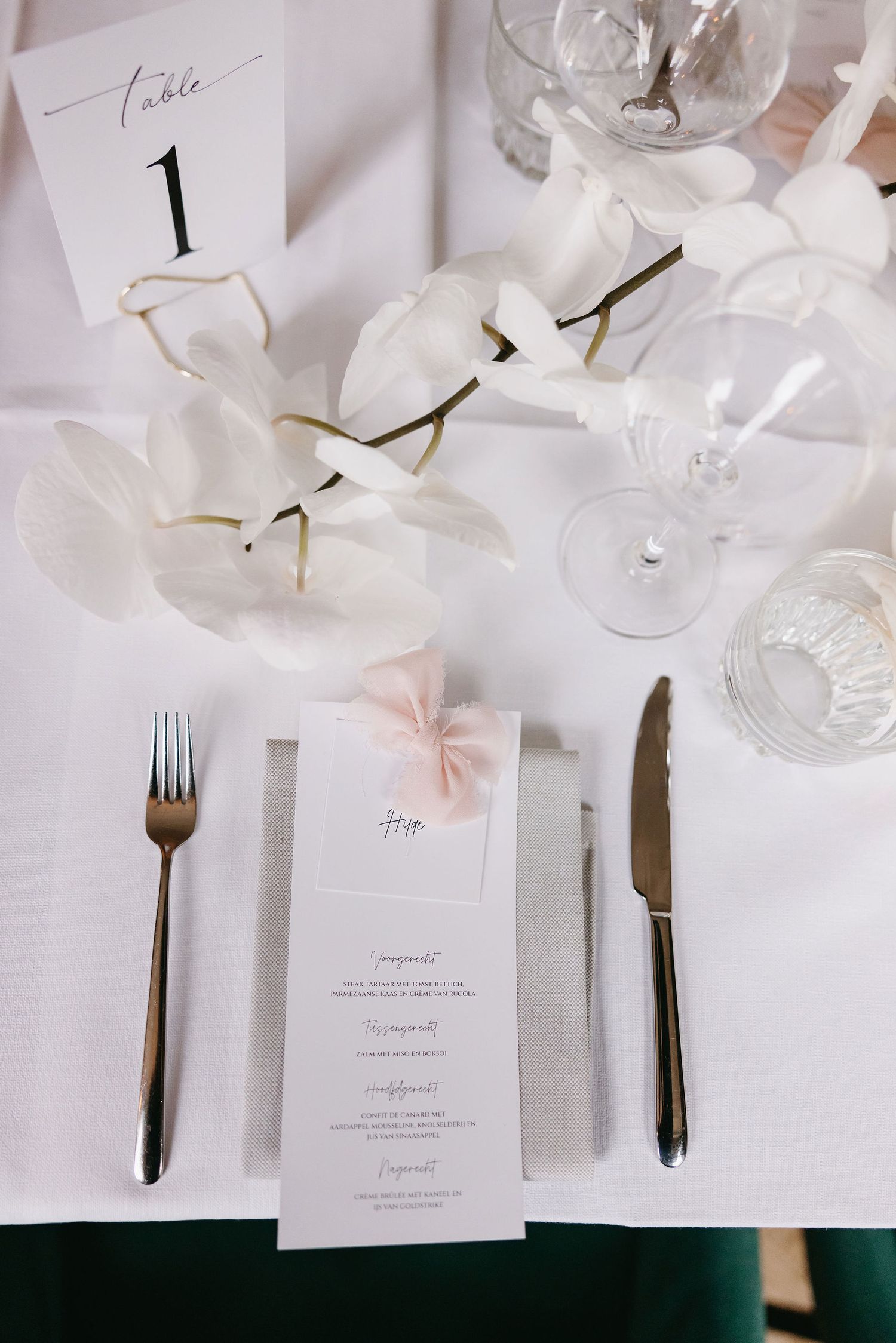 White wedding reception table setting with elegant place cards, cutlery, and delicate floral decorations.