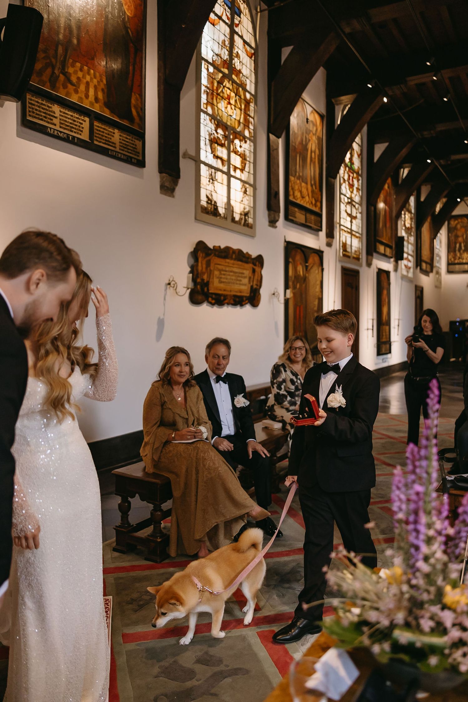 Wedding ceremony moment in historic hall with stained glass windows and unexpected dog appearance.