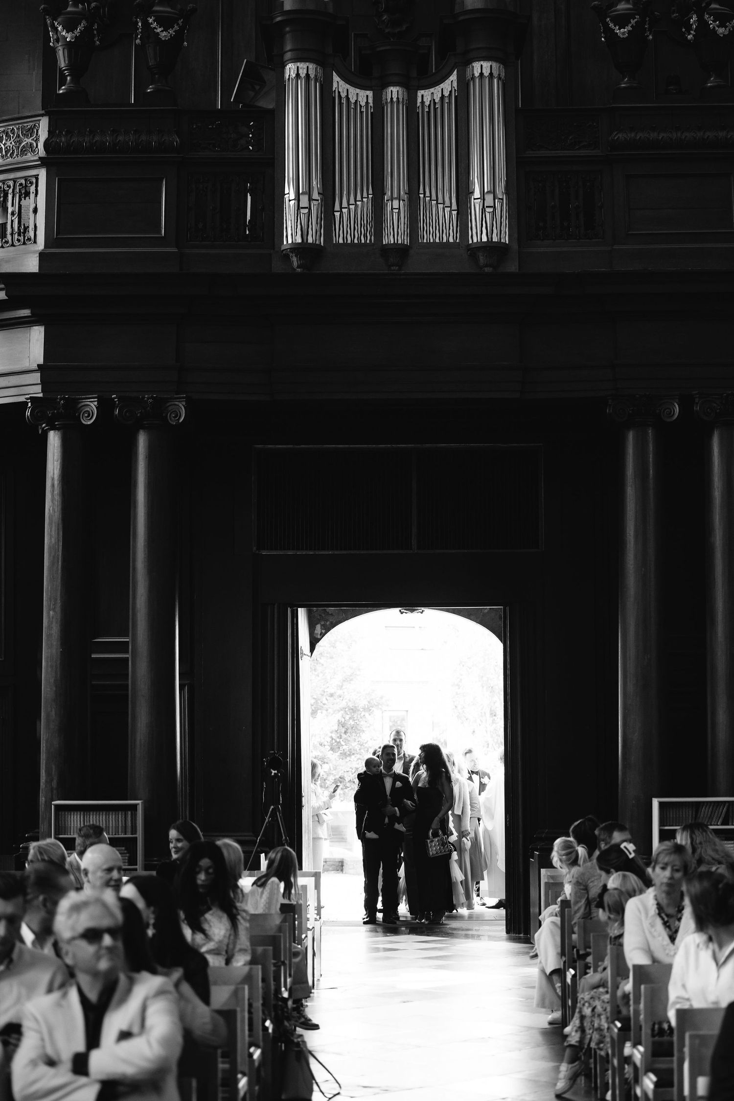 Wedding guests watch as silhouettes appear in church doorway during ceremony.