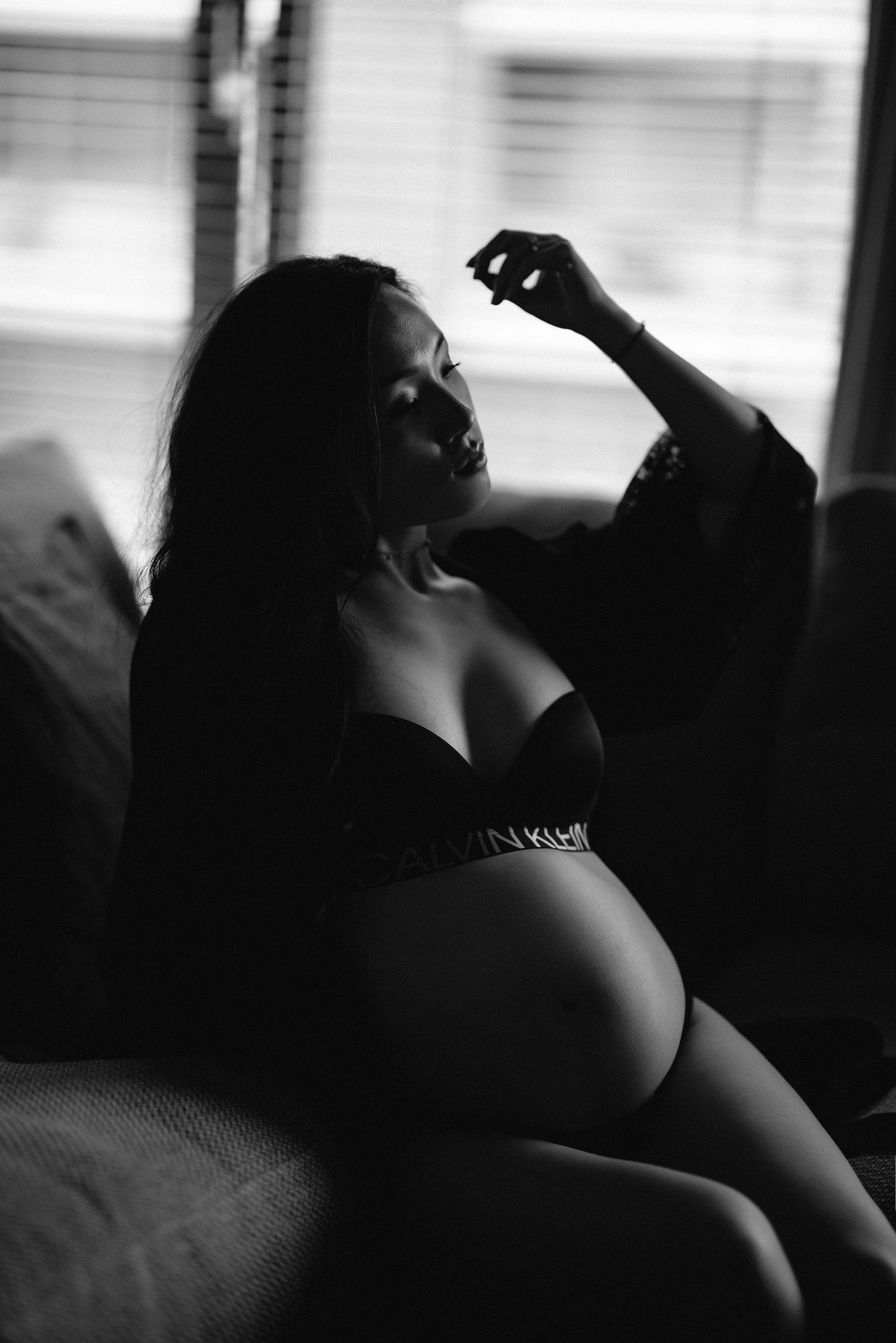 Artistic black and white boudoir maternity photo in silhouette by window.