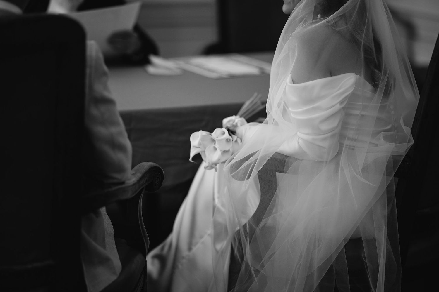 A black and white wedding photo showing delicate tulle fabric and formal attire during a ceremony.