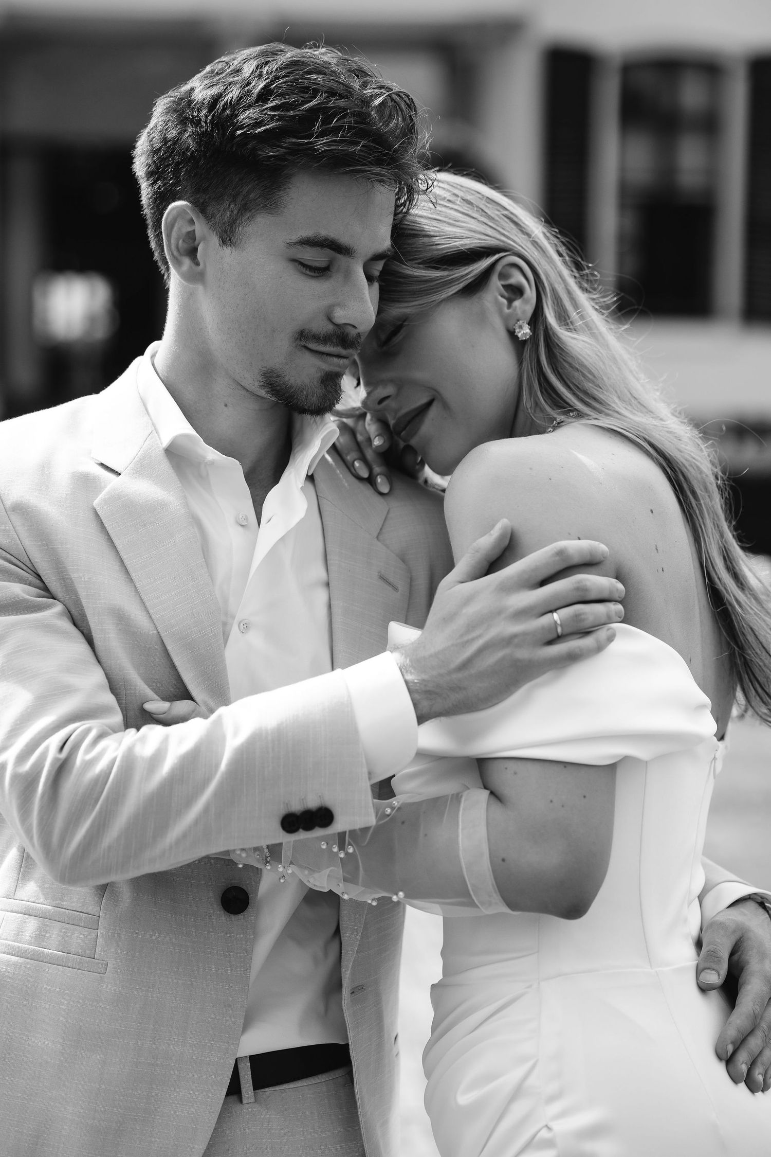 Intimate black and white portrait of newlyweds sharing a tender moment in elegant white attire.