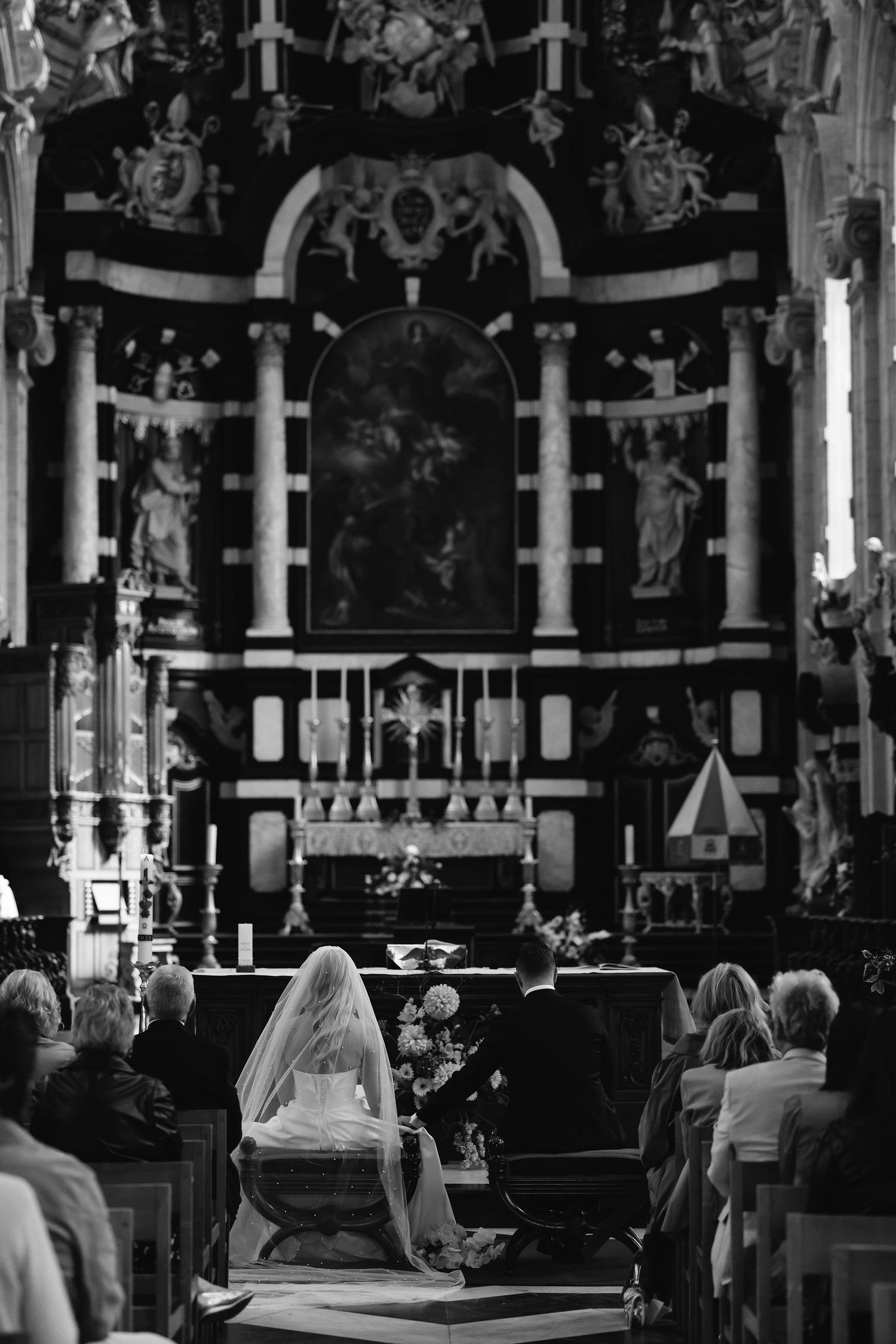 Black and white photograph of a church interior during a ceremony with ornate baroque altar and gathered congregation.