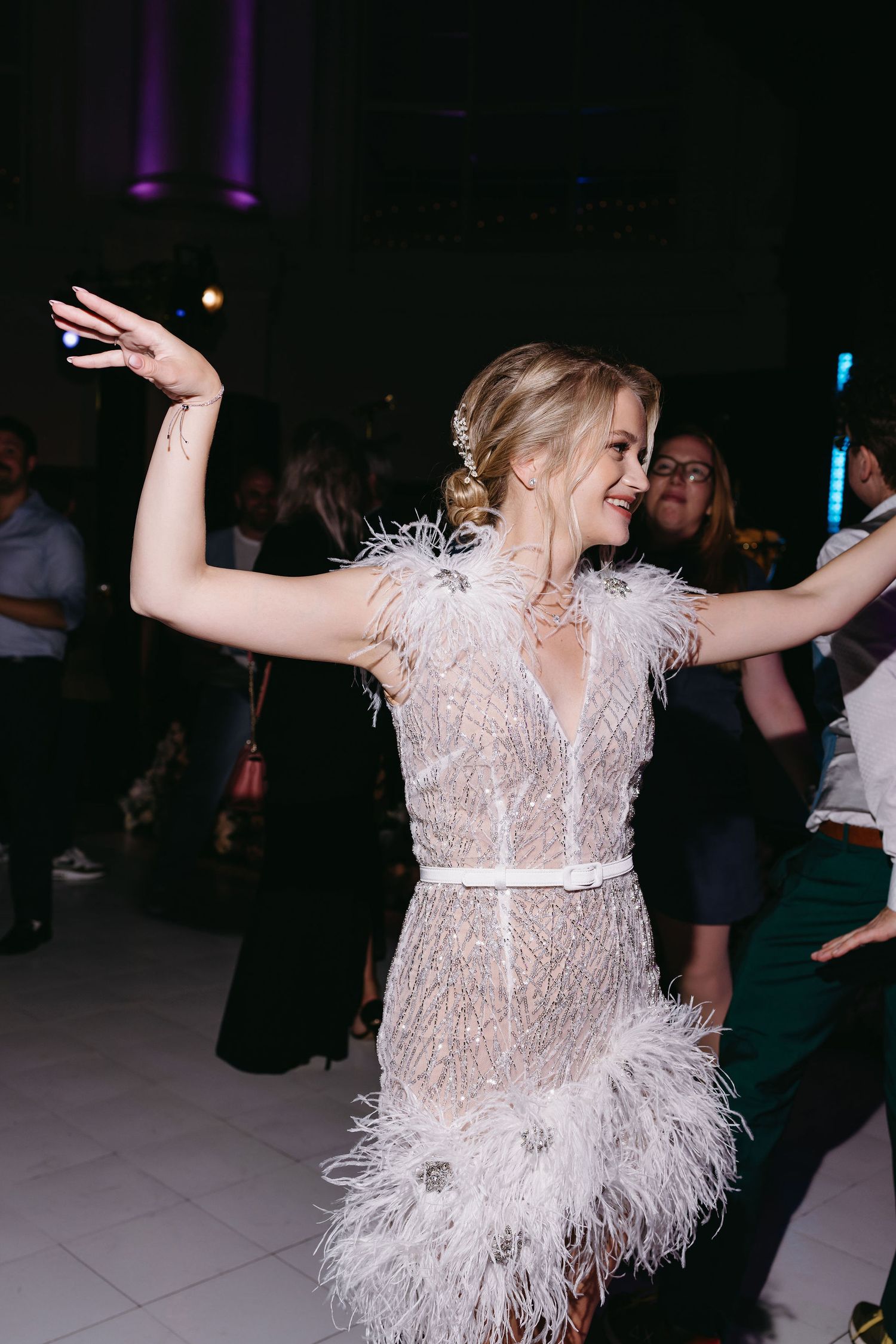 Dancing at wedding reception in feathered white dress with purple lighting.