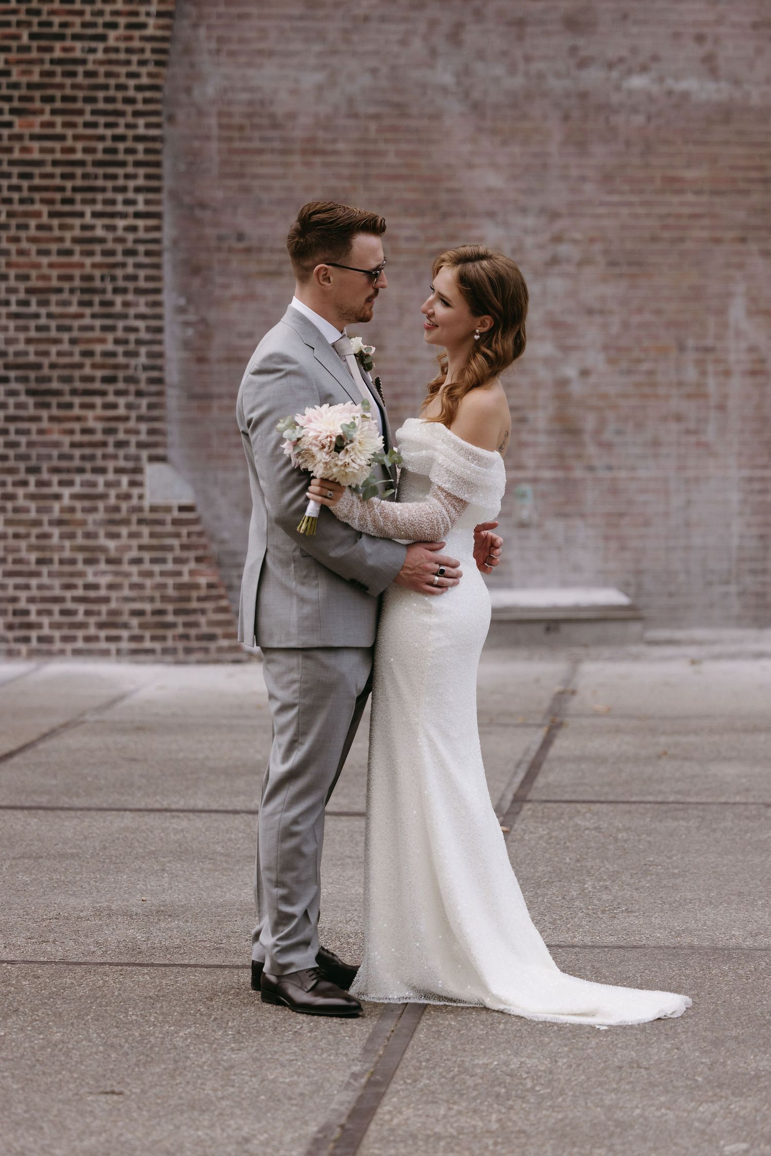 A romantic first look moment between newlyweds against a brick wall backdrop.