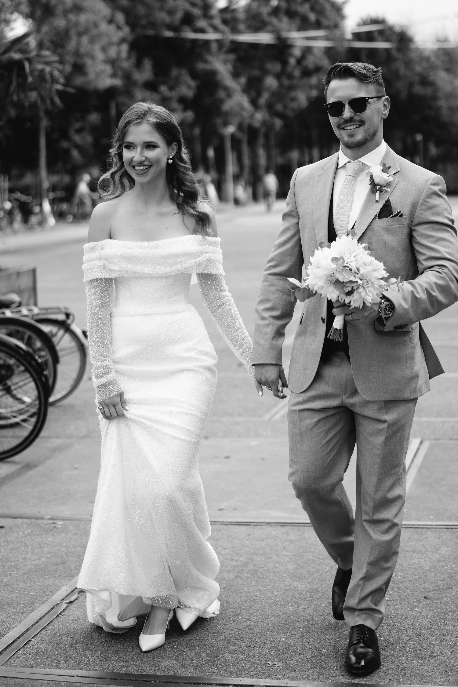 A black and white portrait of newlyweds walking together outdoors on their wedding day.