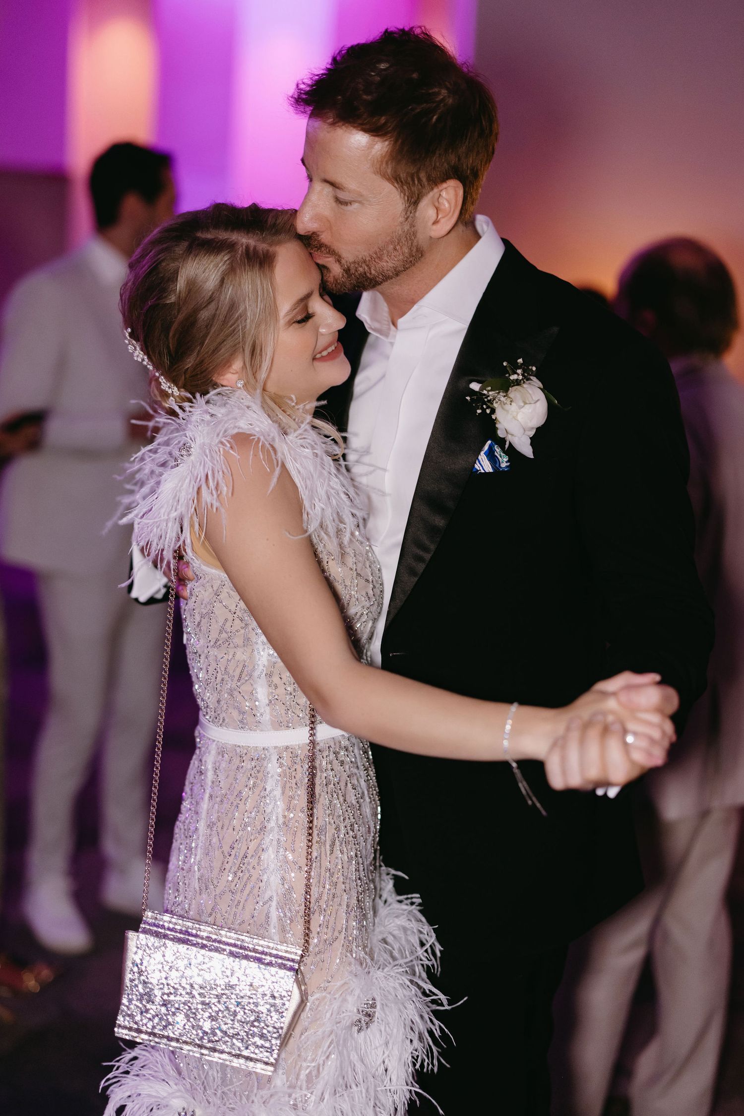 Couple dancing at a wedding reception with the bride wearing a feathered white dress.