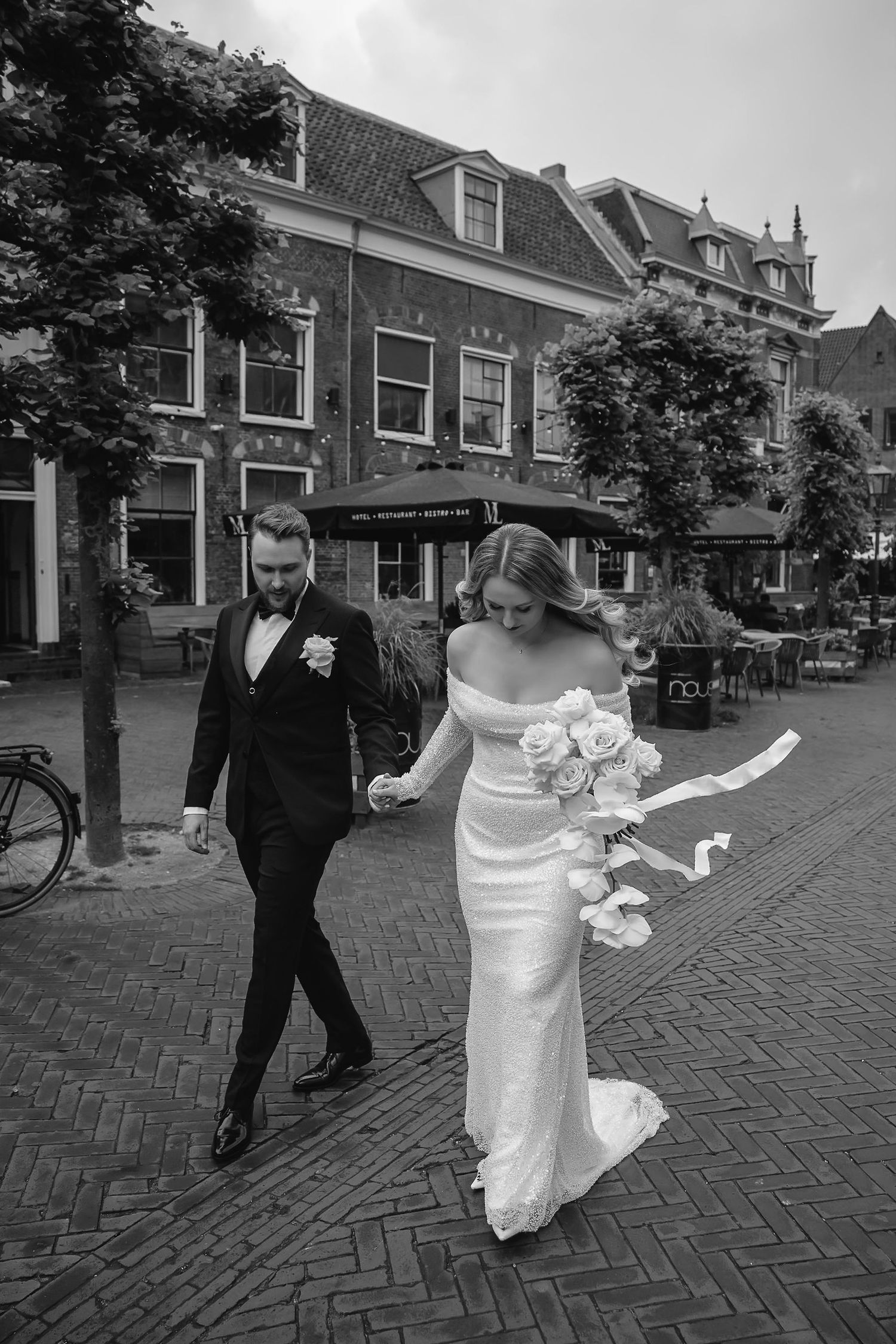 Bride and groom walking together on cobblestone street in European city setting.