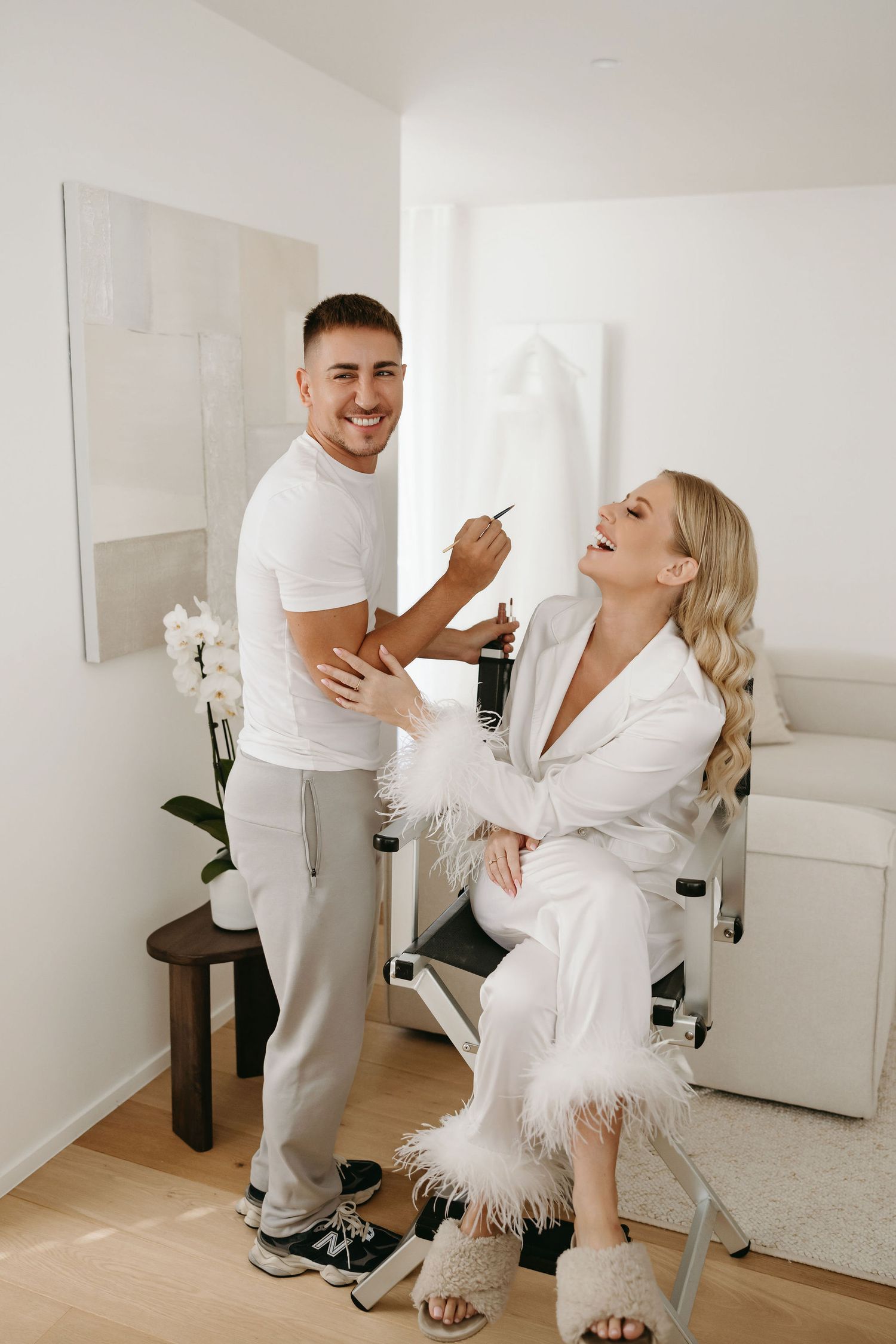 Behind the scenes wedding preparation showing makeup application in bright white room.
