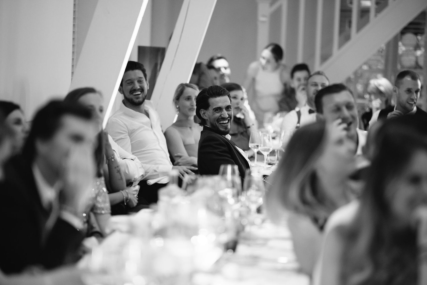 Wedding reception guests laughing and socializing at elegantly set dinner tables.