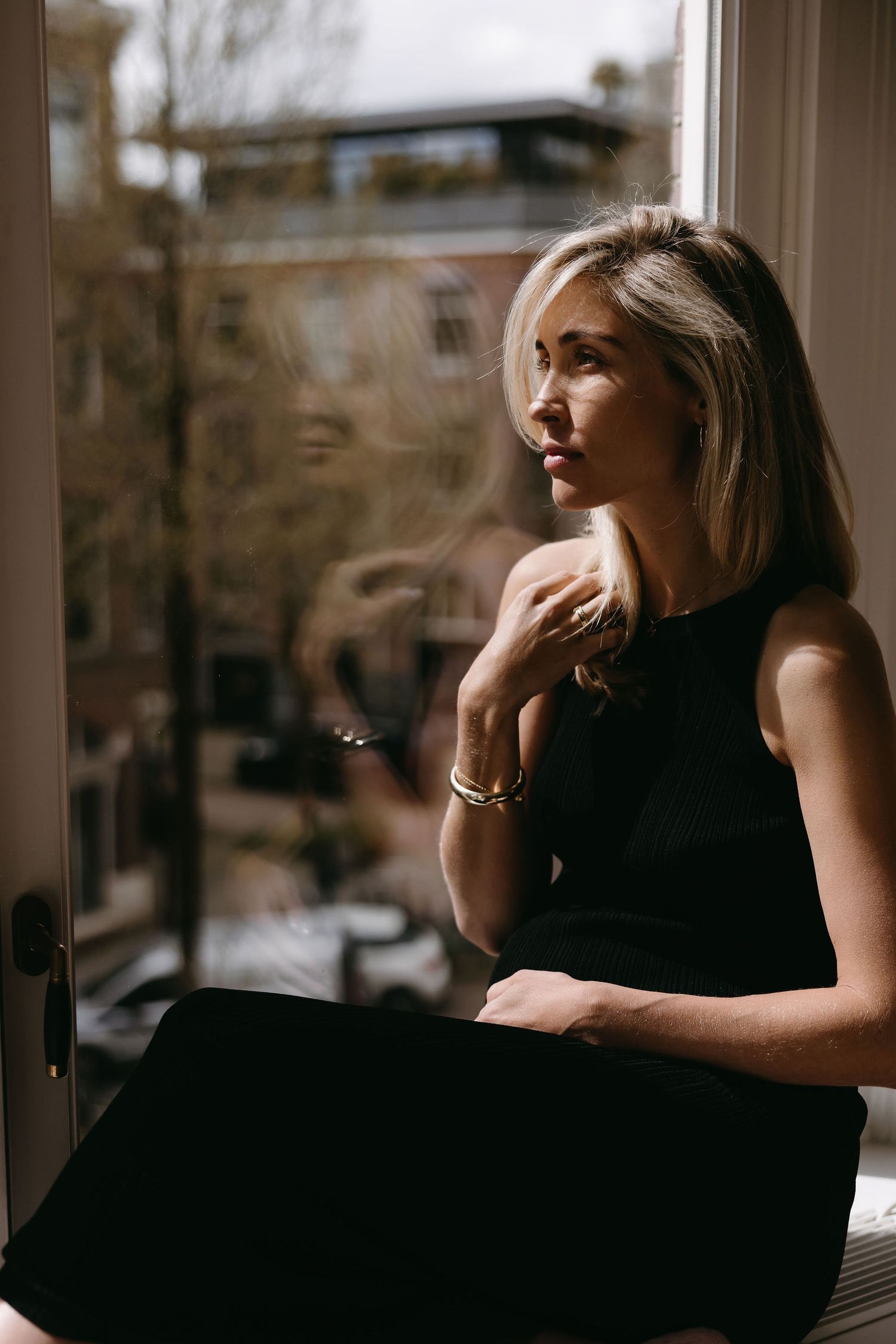 Contemplative portrait by window with soft natural lighting and urban view.