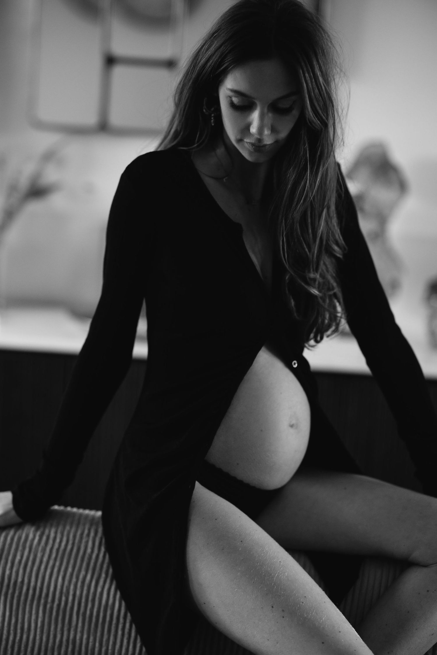 Artistic maternity photo showing pregnant woman in black dress posing on couch.