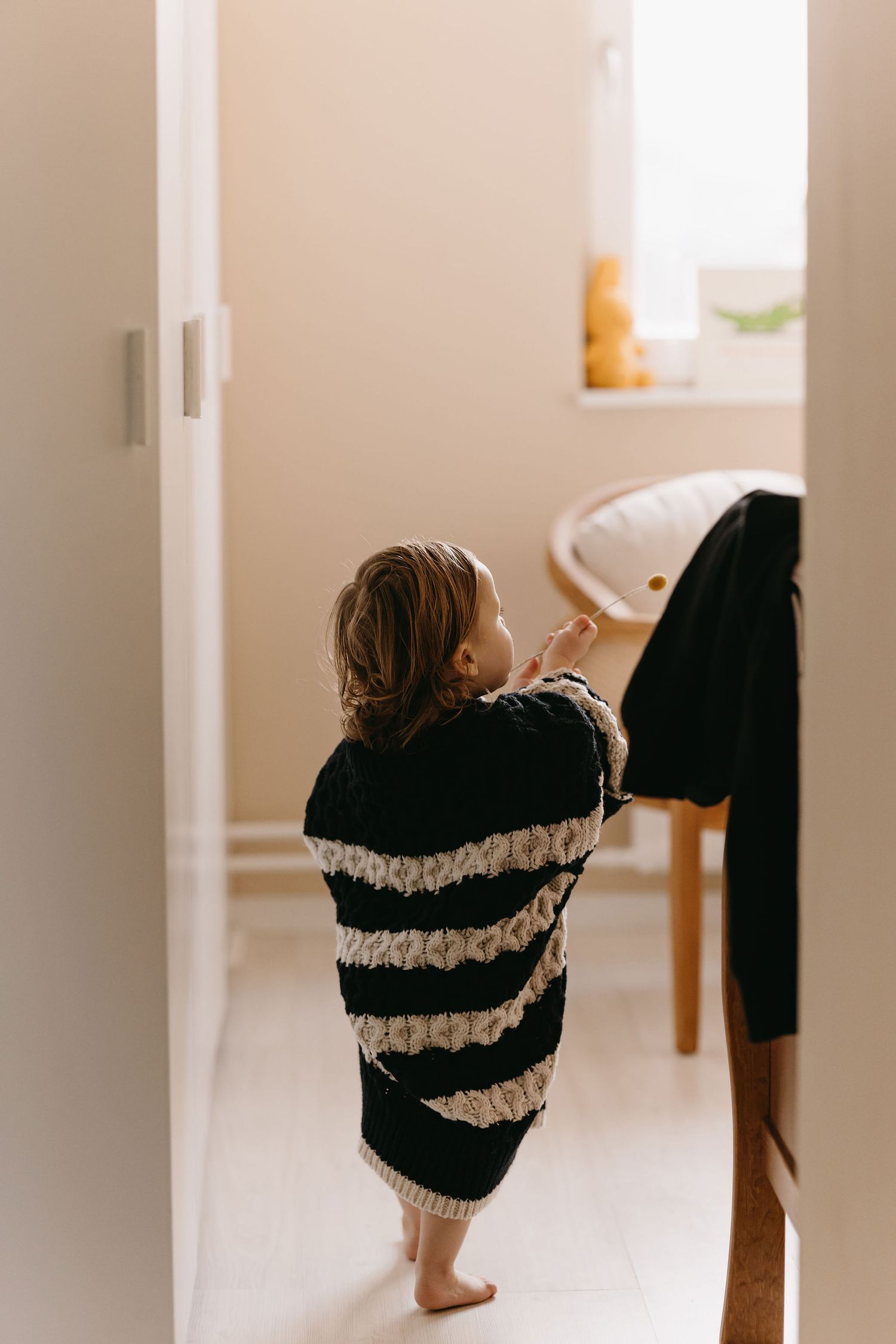 Small child in striped sweater peeks around doorway in candid home photo.