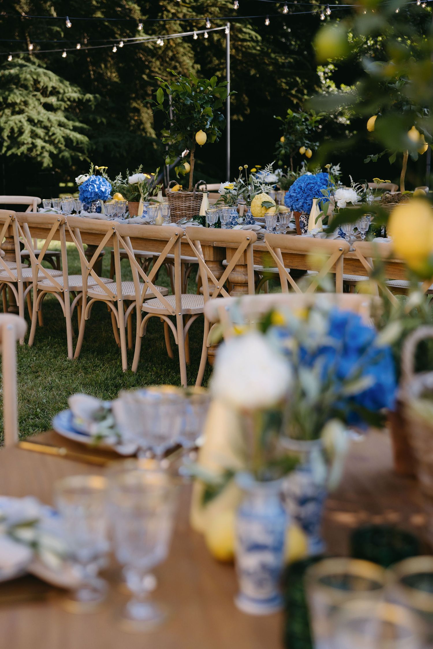 Long wooden tables decorated with blue floral centerpieces at an outdoor wedding reception.