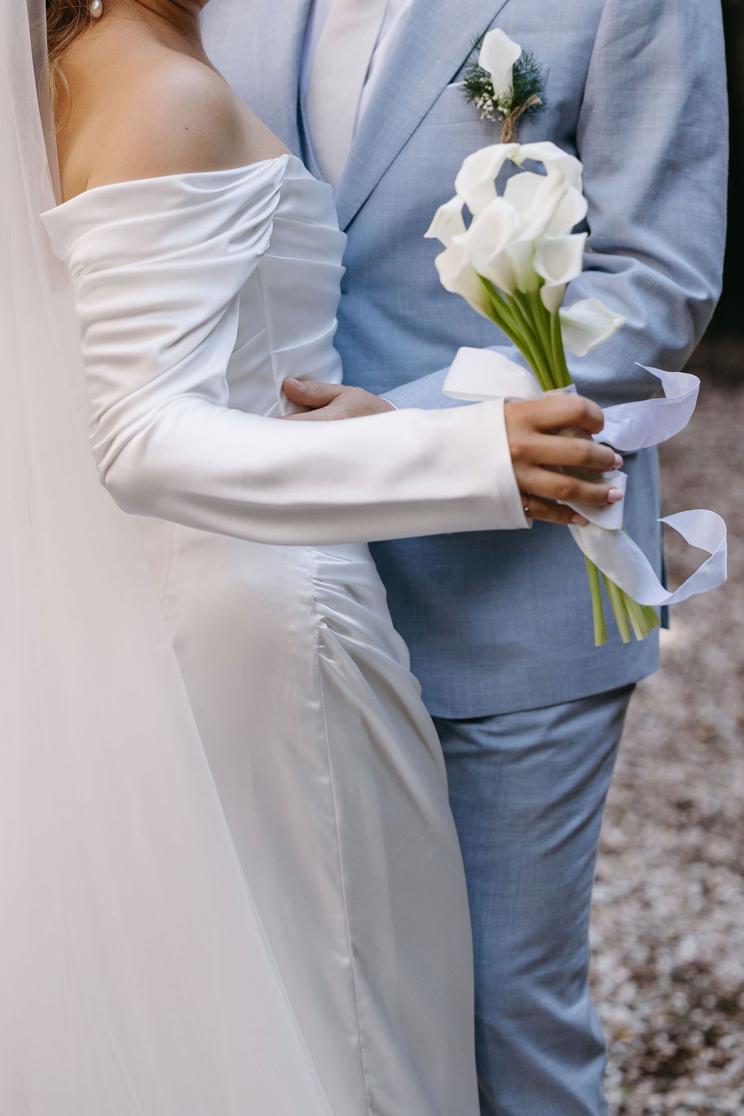 Close-up of wedding couple in white dress and light blue suit holding white calla lilies.