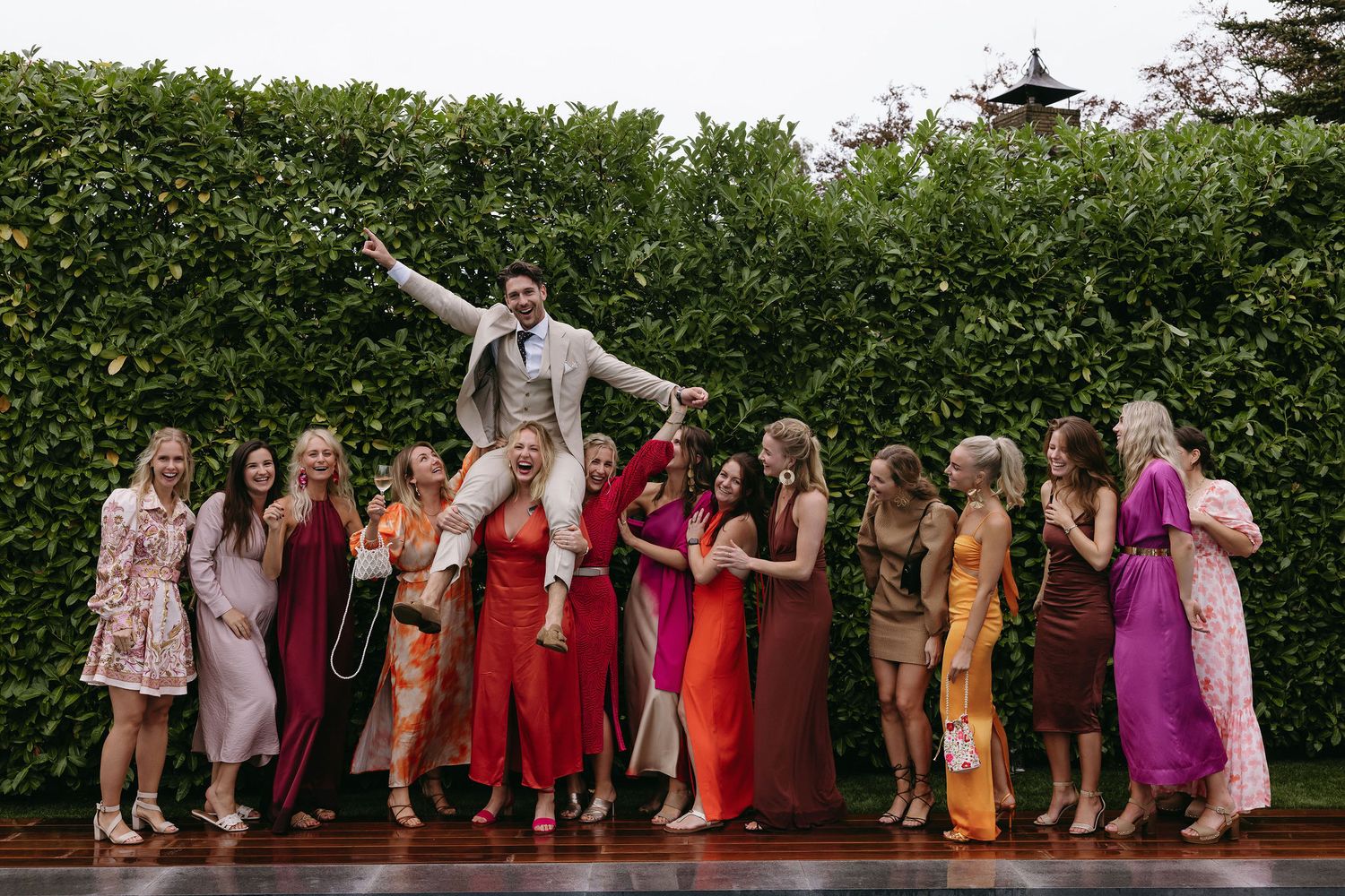Wedding party poses with bridesmaids in colorful dresses on an outdoor patio during celebration.