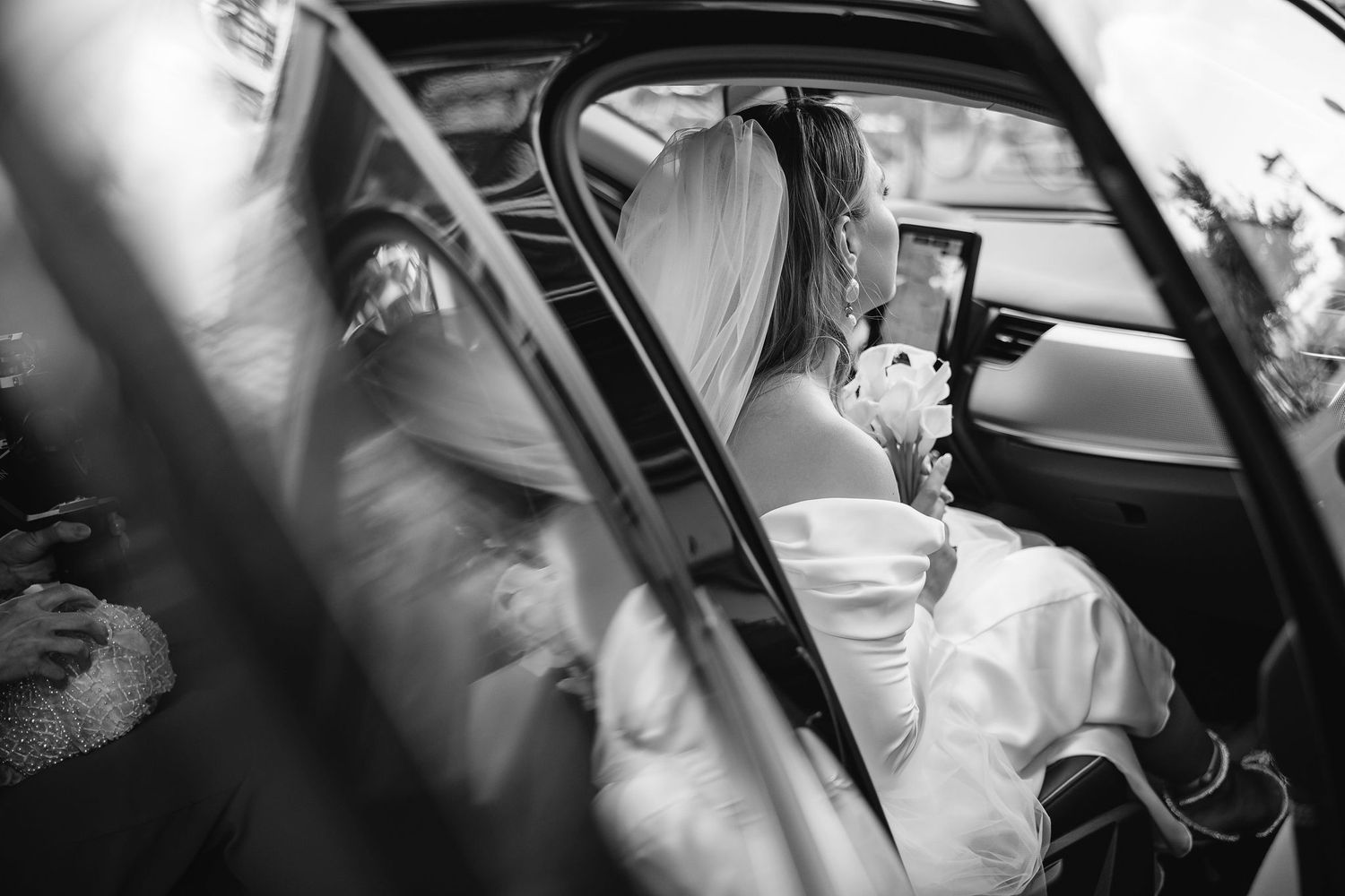Black and white photo of bride in wedding dress seated in vintage car.