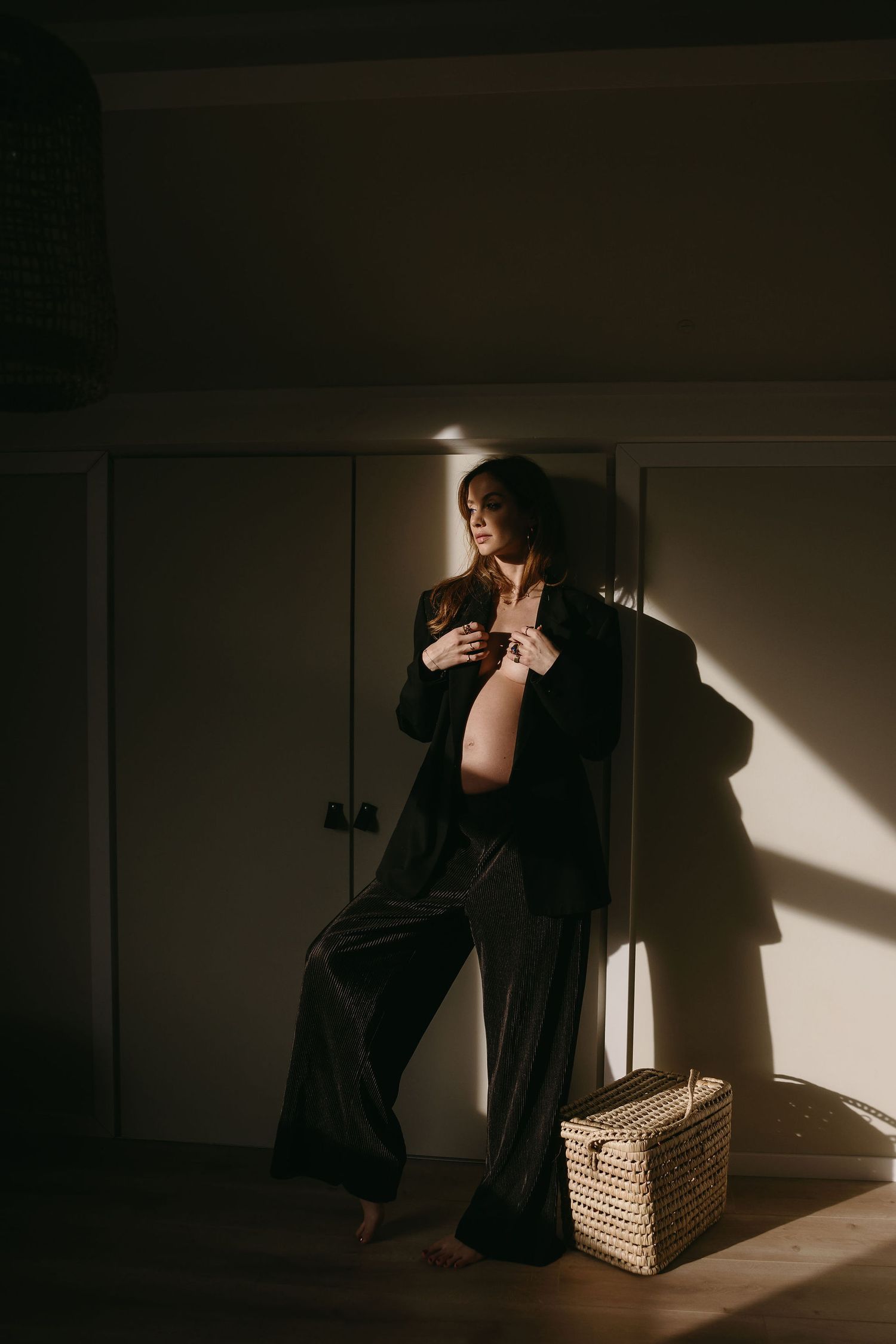 Dramatic shadows and light play across figure sitting in dark room with woven basket.
