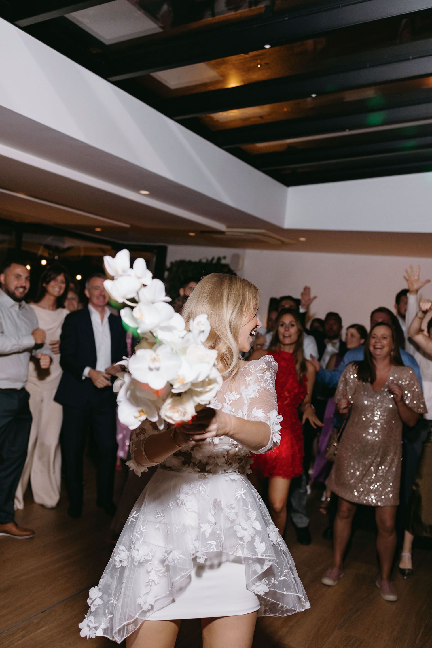 Wedding reception with dancing and white floral bouquet in a venue with dark ceiling beams.