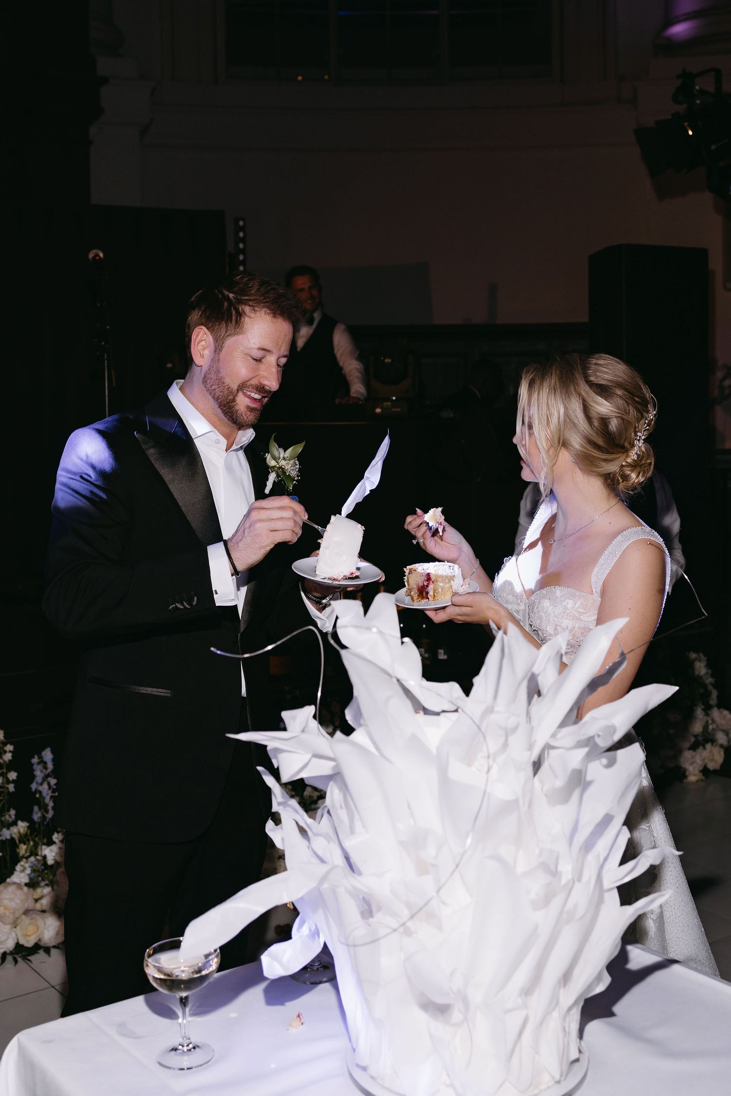 Couple shares a playful moment while cutting their wedding cake decorated with white sculptural elements.