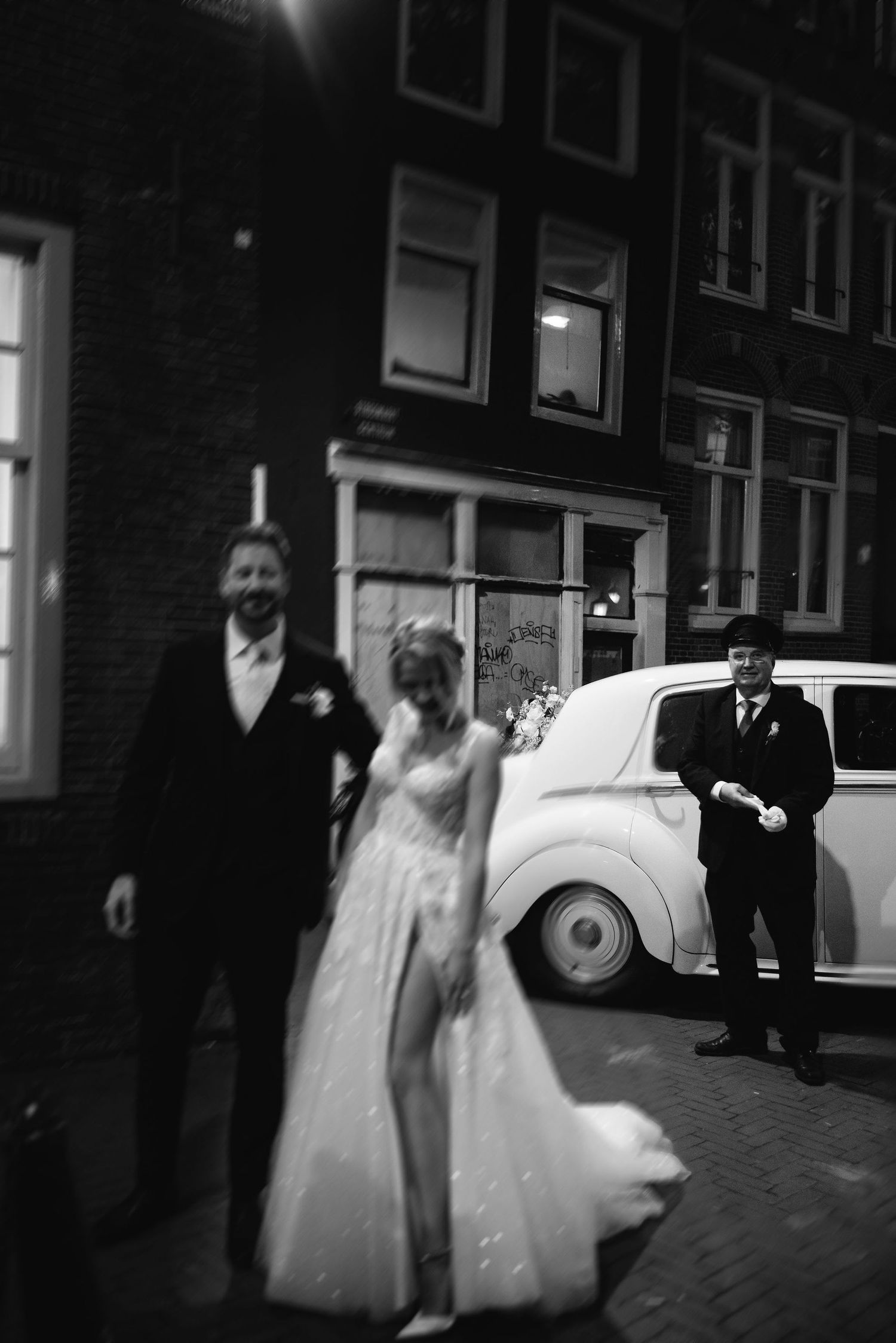 Black and white wedding photos showing a couple exiting near a classic car on a brick street.