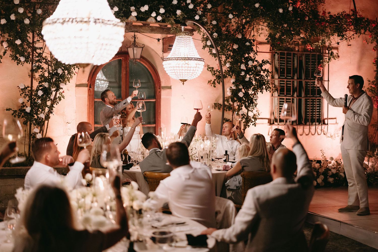 Romantic outdoor wedding reception at night with string lights illuminating tables and guests in a garden setting.