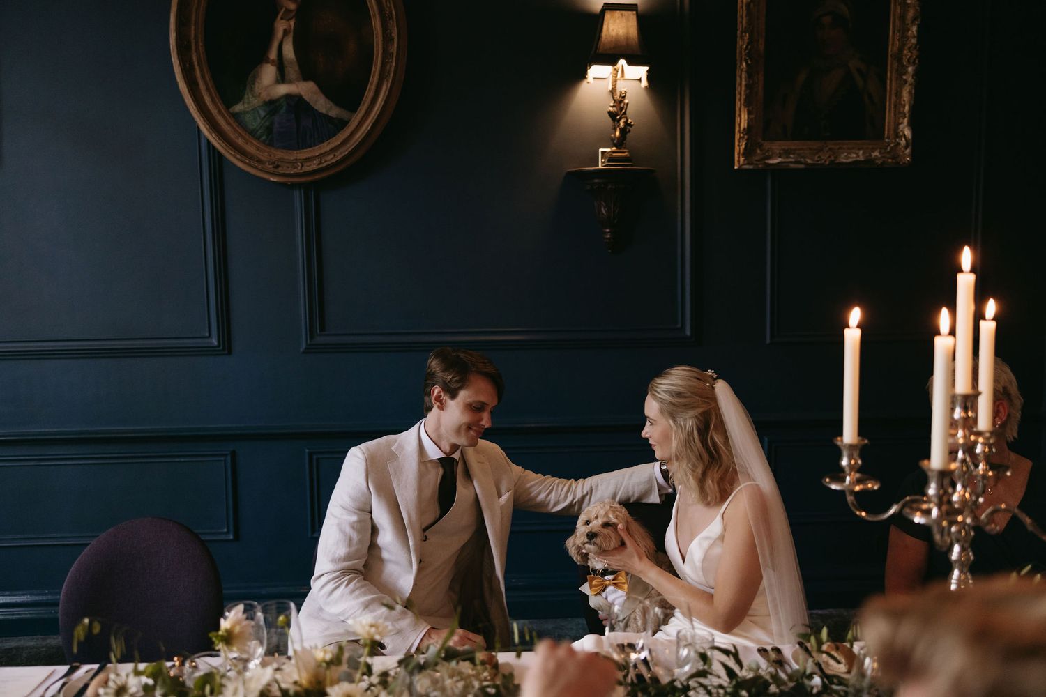 Elegant wedding reception setting with candelabras and dark blue walls in dramatic lighting.