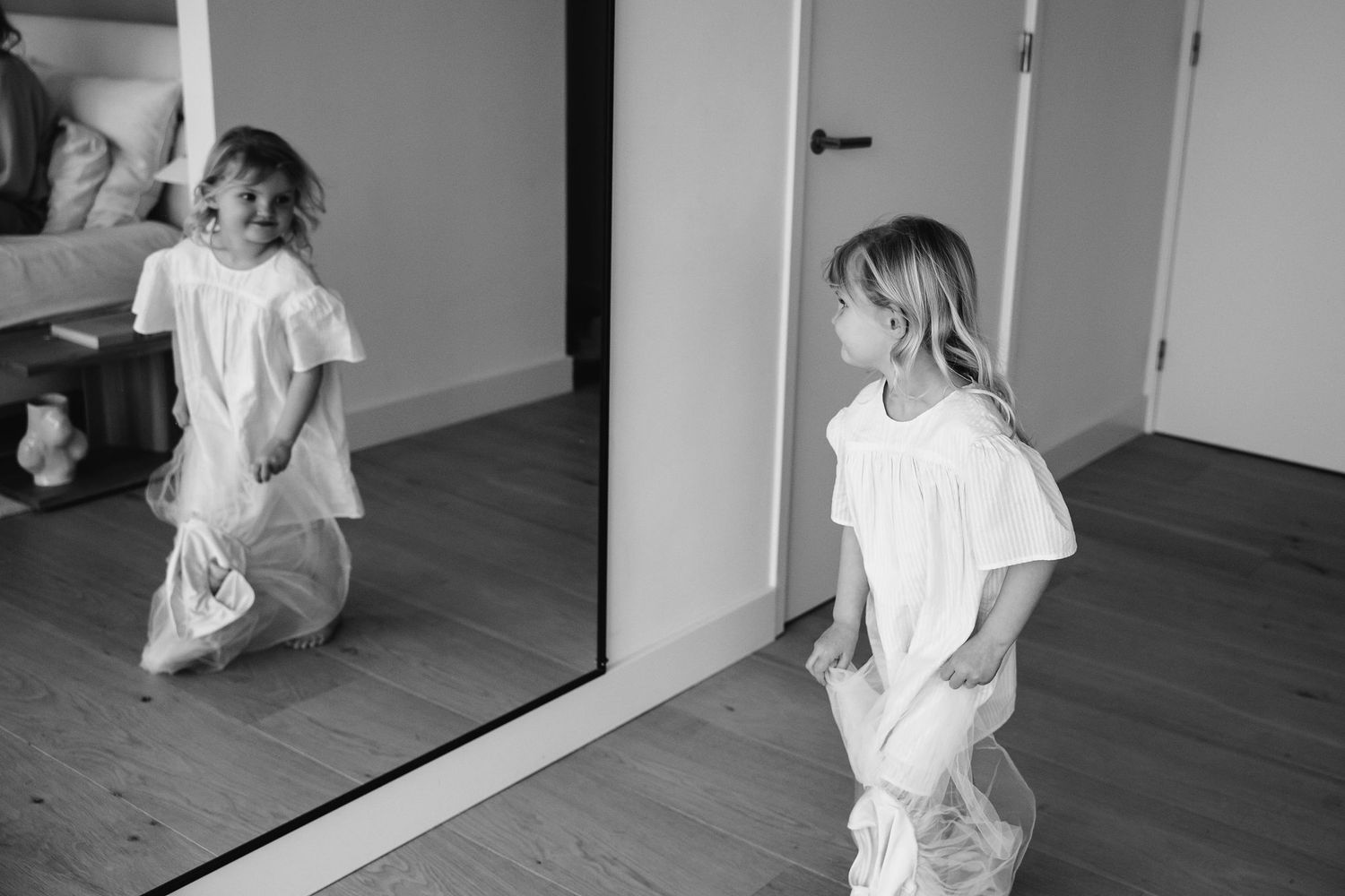 A child dances joyfully in front of a full-length mirror in black and white.