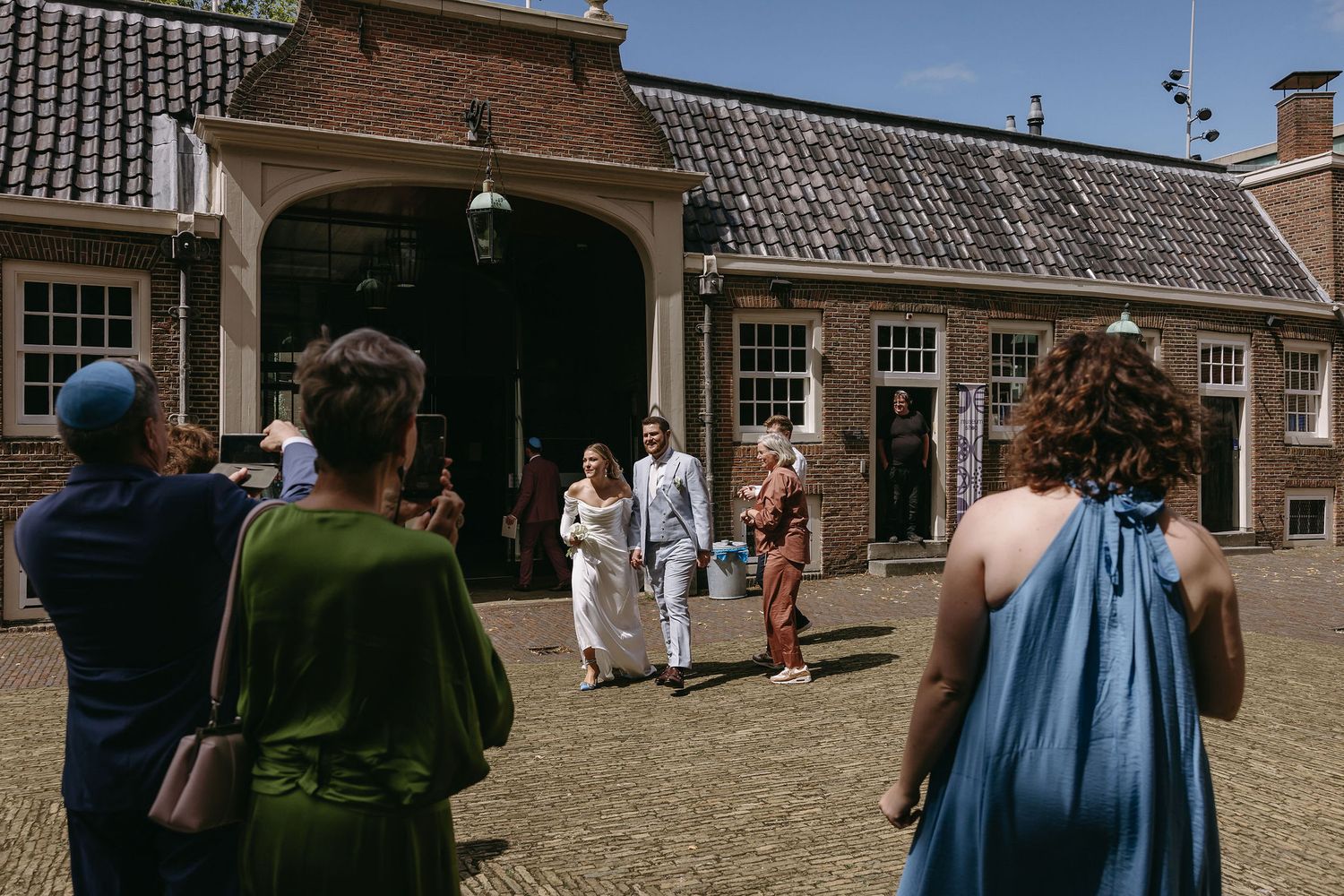 Outdoor gathering at historic brick building with people in casual attire mingling in courtyard.