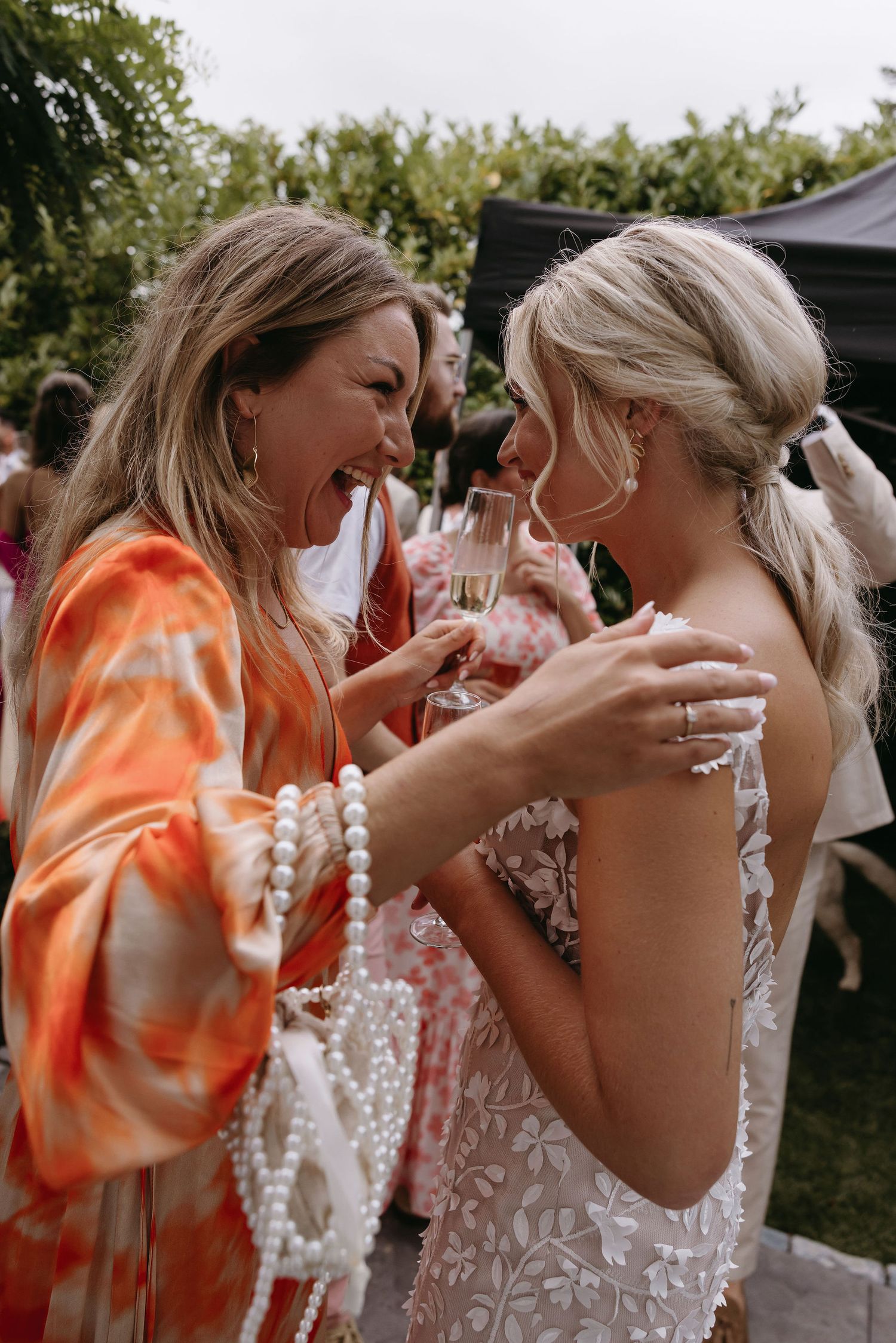 Emotional moments shared between wedding attendees in white lace and orange floral dresses.