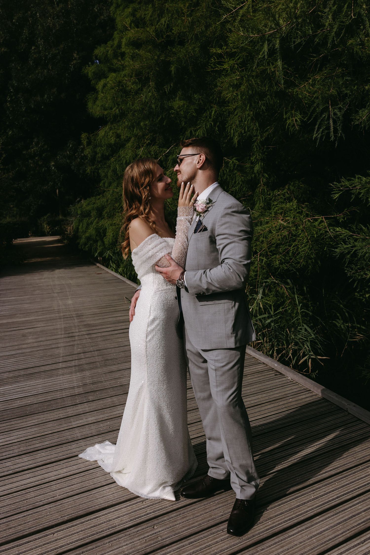 Newlyweds share an intimate moment on a wooden boardwalk surrounded by lush greenery.