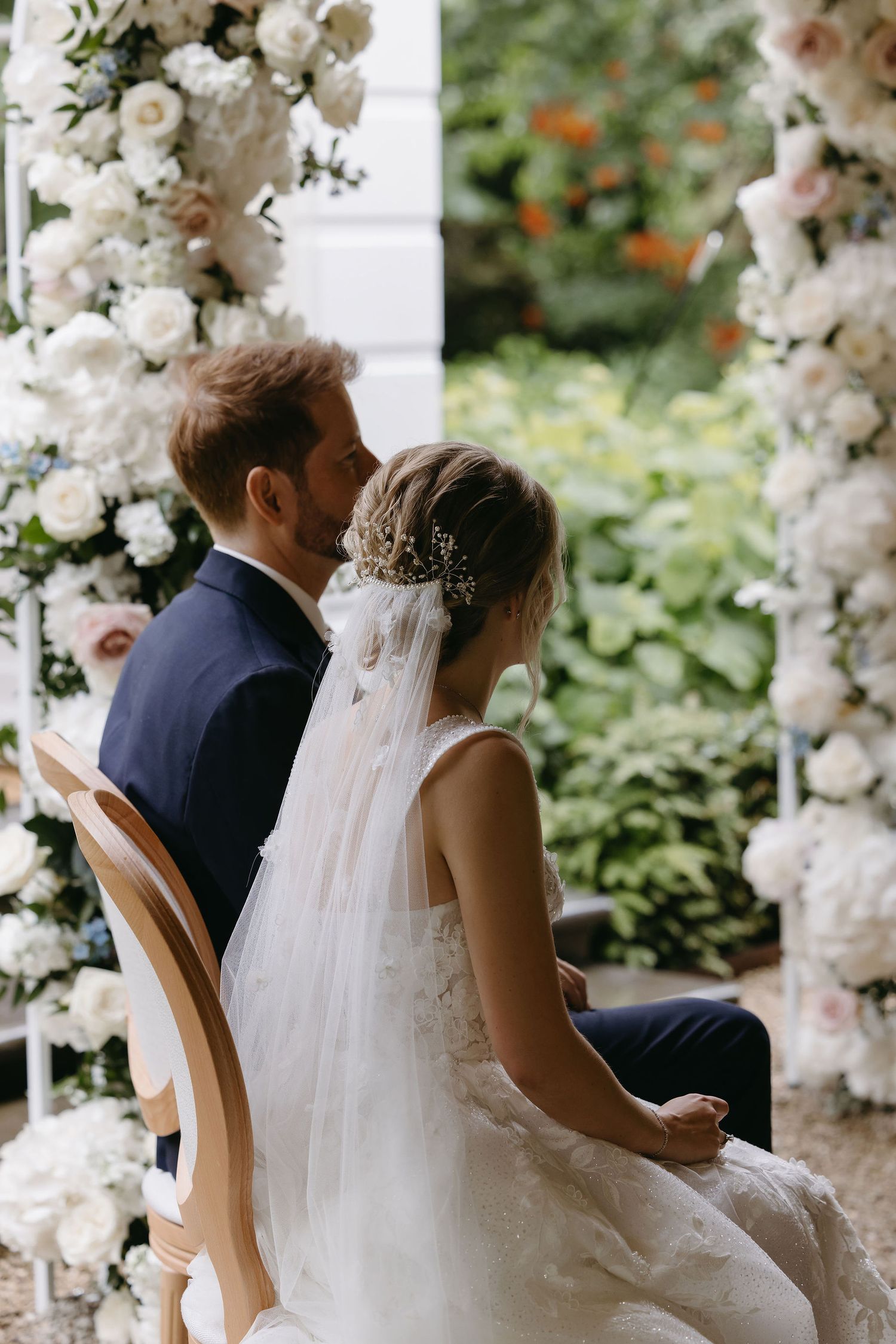 Wedding ceremony setting with white floral arches and garden backdrop.