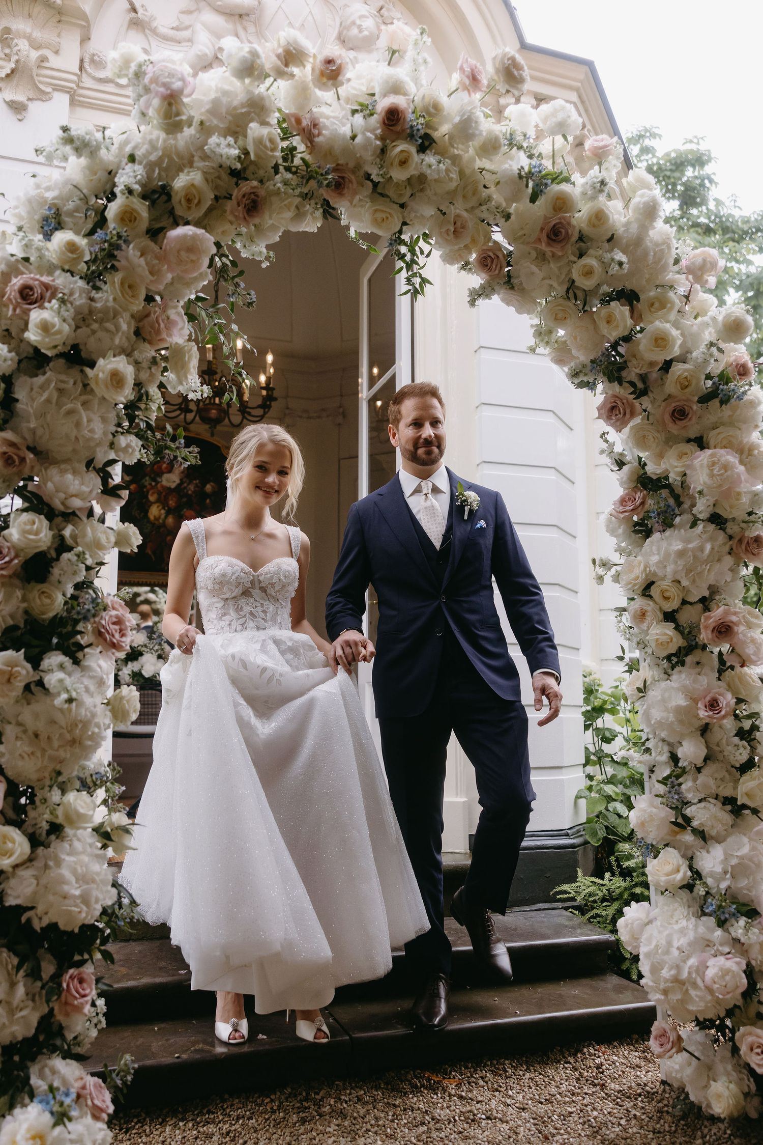 Newlyweds exit under stunning white floral arch after wedding ceremony.