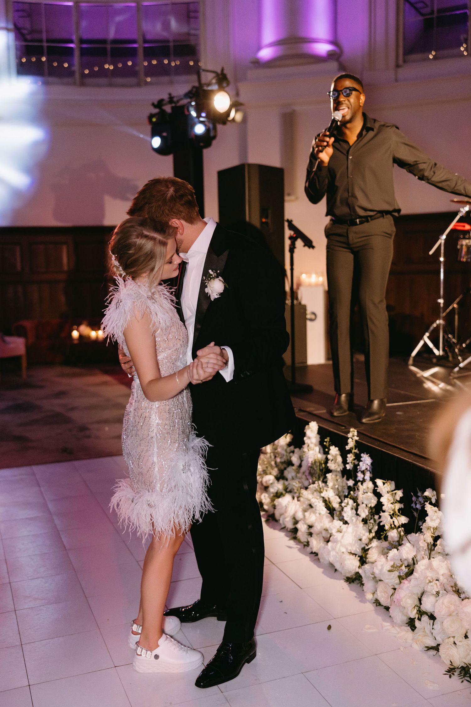 Wedding couple dancing in front of a live band with white floral decorations on a dance floor.