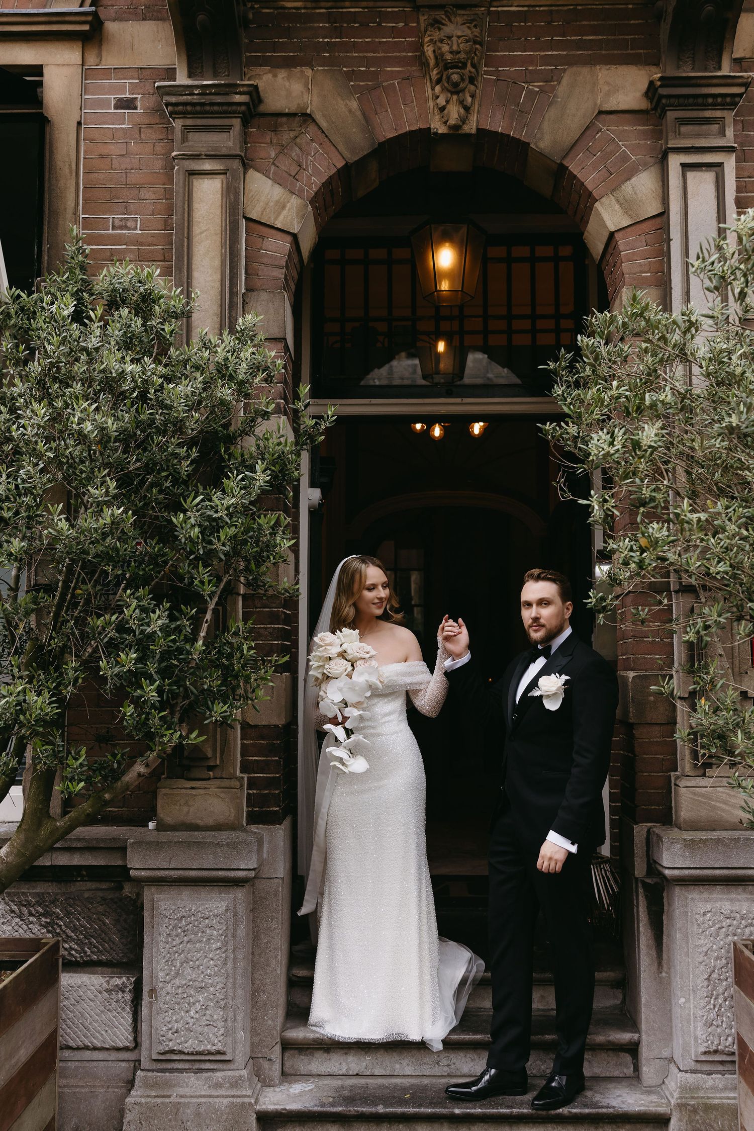 Wedding couple posing outside historic brick building with arched doorways.