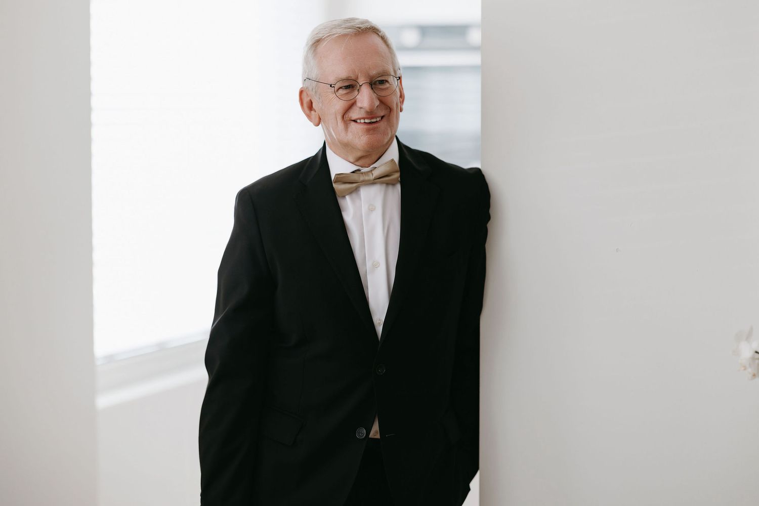 Elegant senior gentleman in formal black tuxedo and bowtie against white wall.