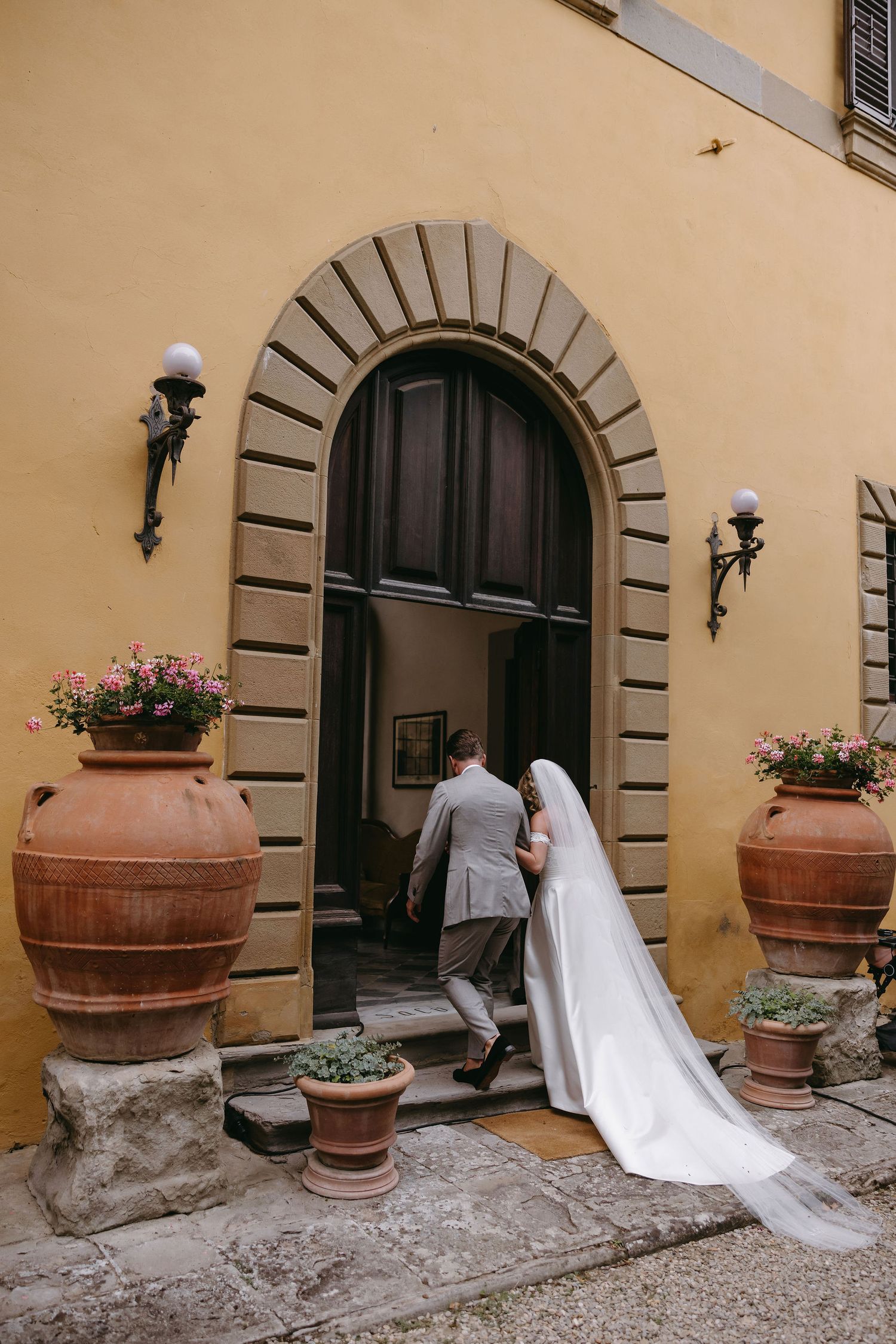A wedding couple entering through an arched doorway of a Mediterranean style building.
